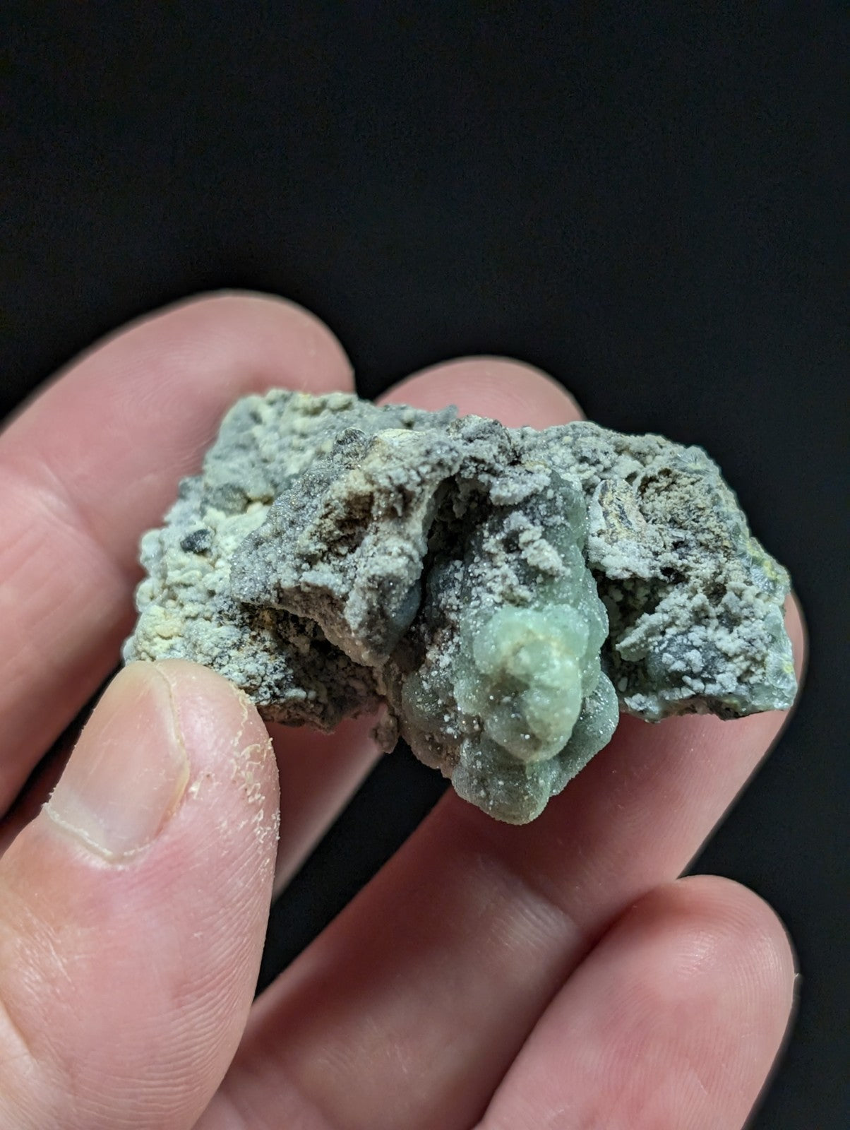 A rough, pale green mineral specimen with a textured surface and crystalline formations.