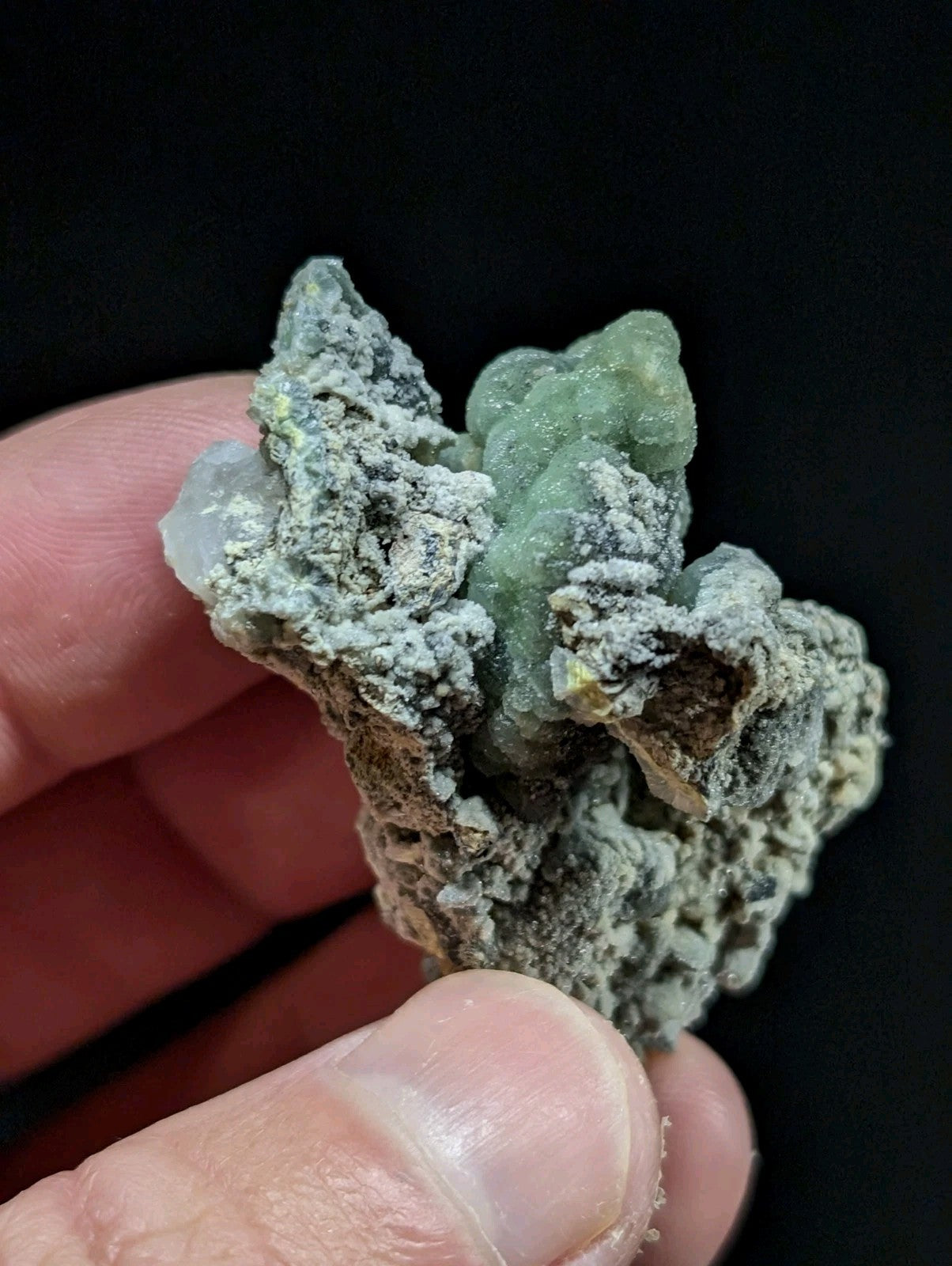 A textured, greenish mineral specimen with a rough, crystalline surface and patches of white coating.
