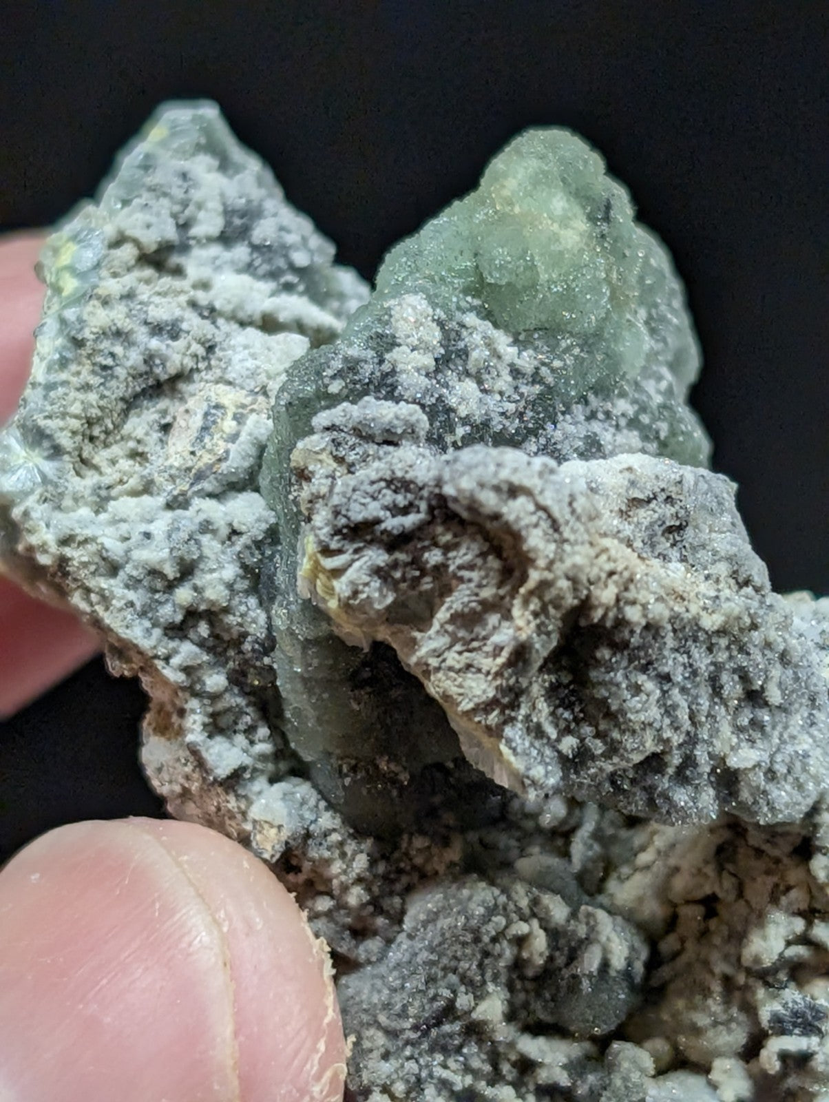 A rough, irregularly shaped mineral specimen with a translucent greenish hue and grayish-white crystalline coating.