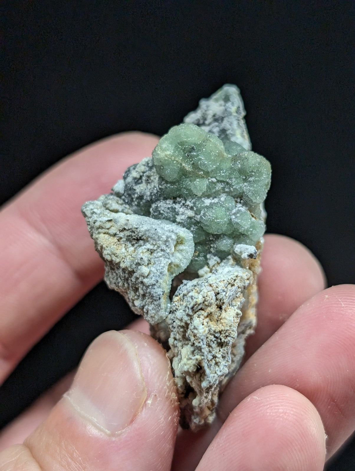 A translucent green mineral specimen with a rough, textured surface and clustered crystalline formations.