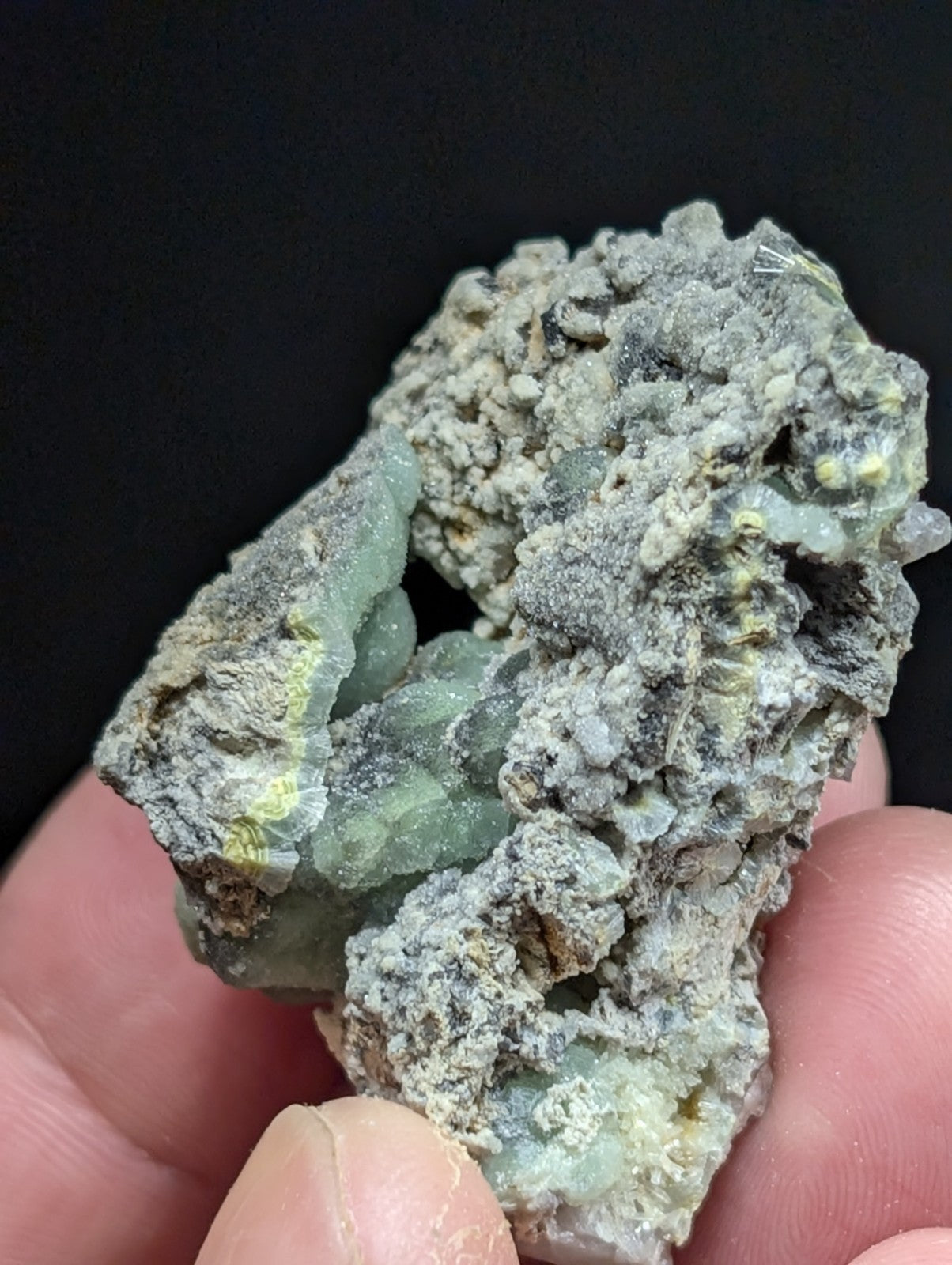 A rough, irregularly shaped mineral specimen with translucent green crystalline formations embedded in a grayish matrix.
