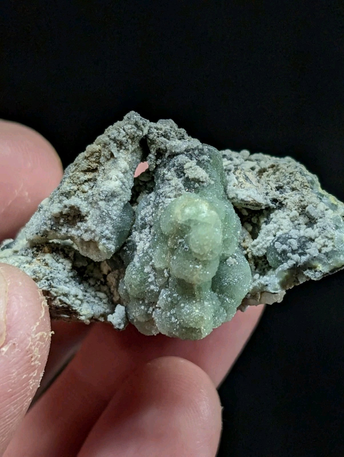 A translucent green mineral specimen with a rough, textured surface and crystalline formations.