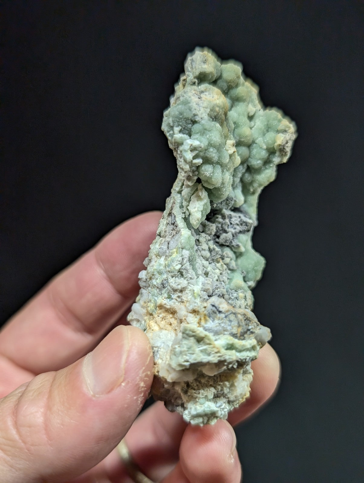 A textured, light green mineral specimen with a rough, bumpy surface and patches of grayish material.