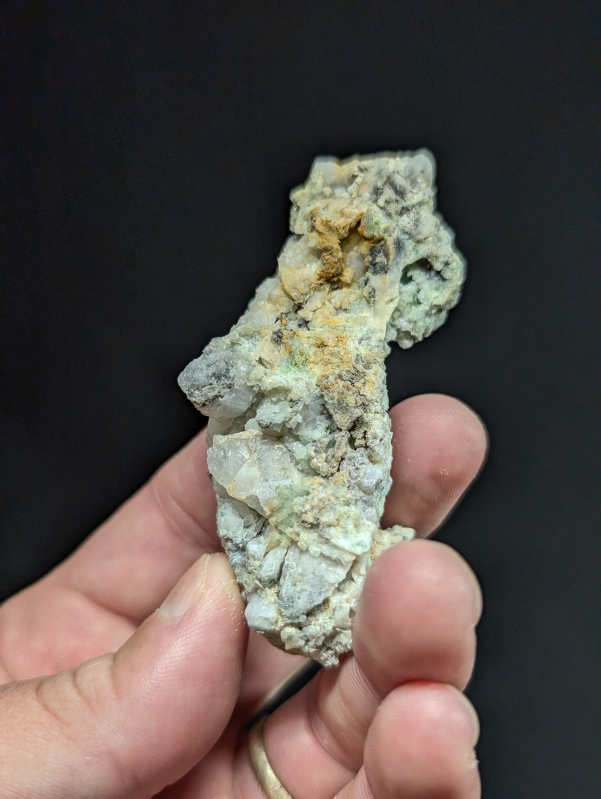 A rough, irregularly shaped mineral specimen with a mottled green and gray surface accented by patches of yellowish-orange.