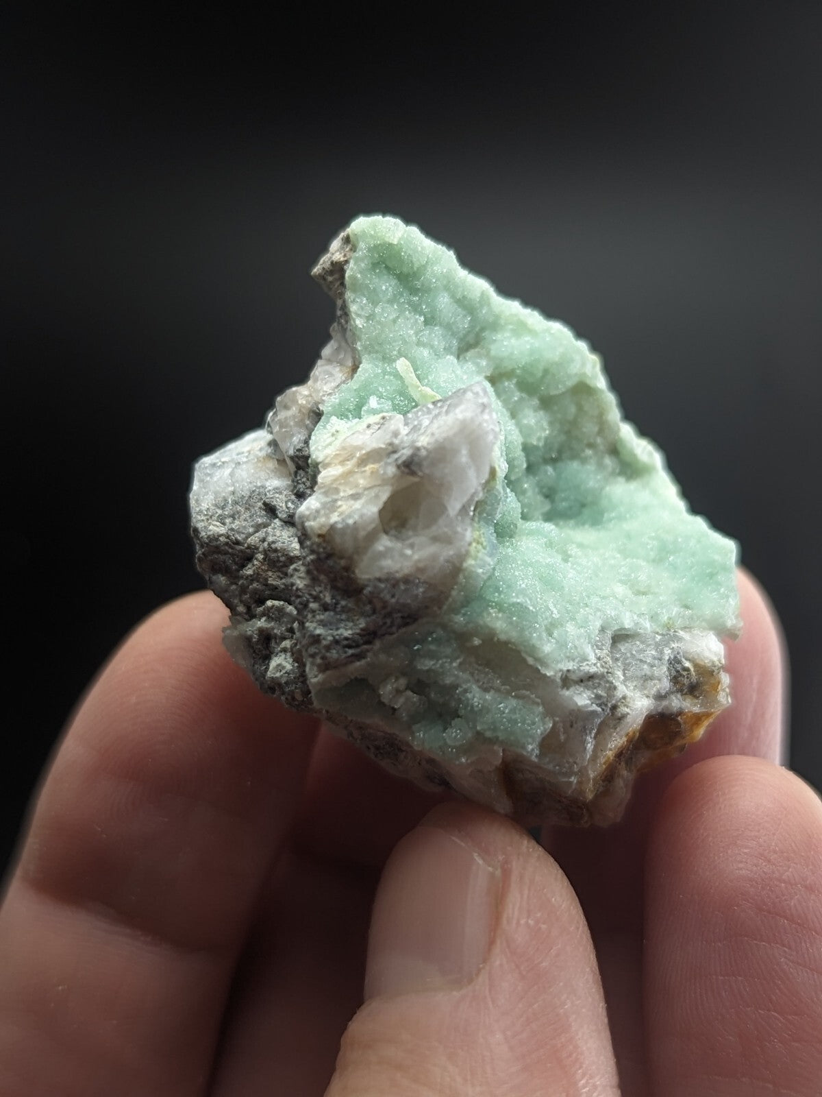 A rough, light green mineral specimen with crystalline textures and grayish matrix material.