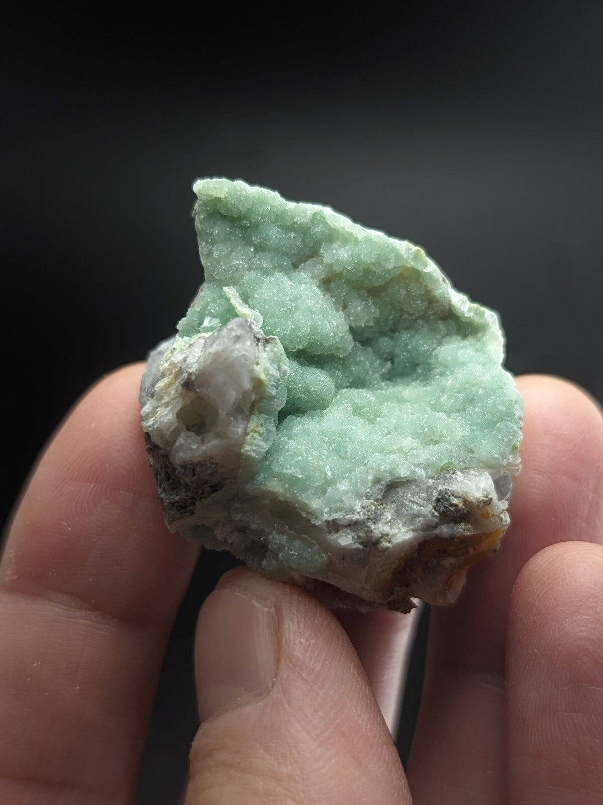 A rough, light green mineral specimen with a crystalline texture and patches of white and gray matrix.