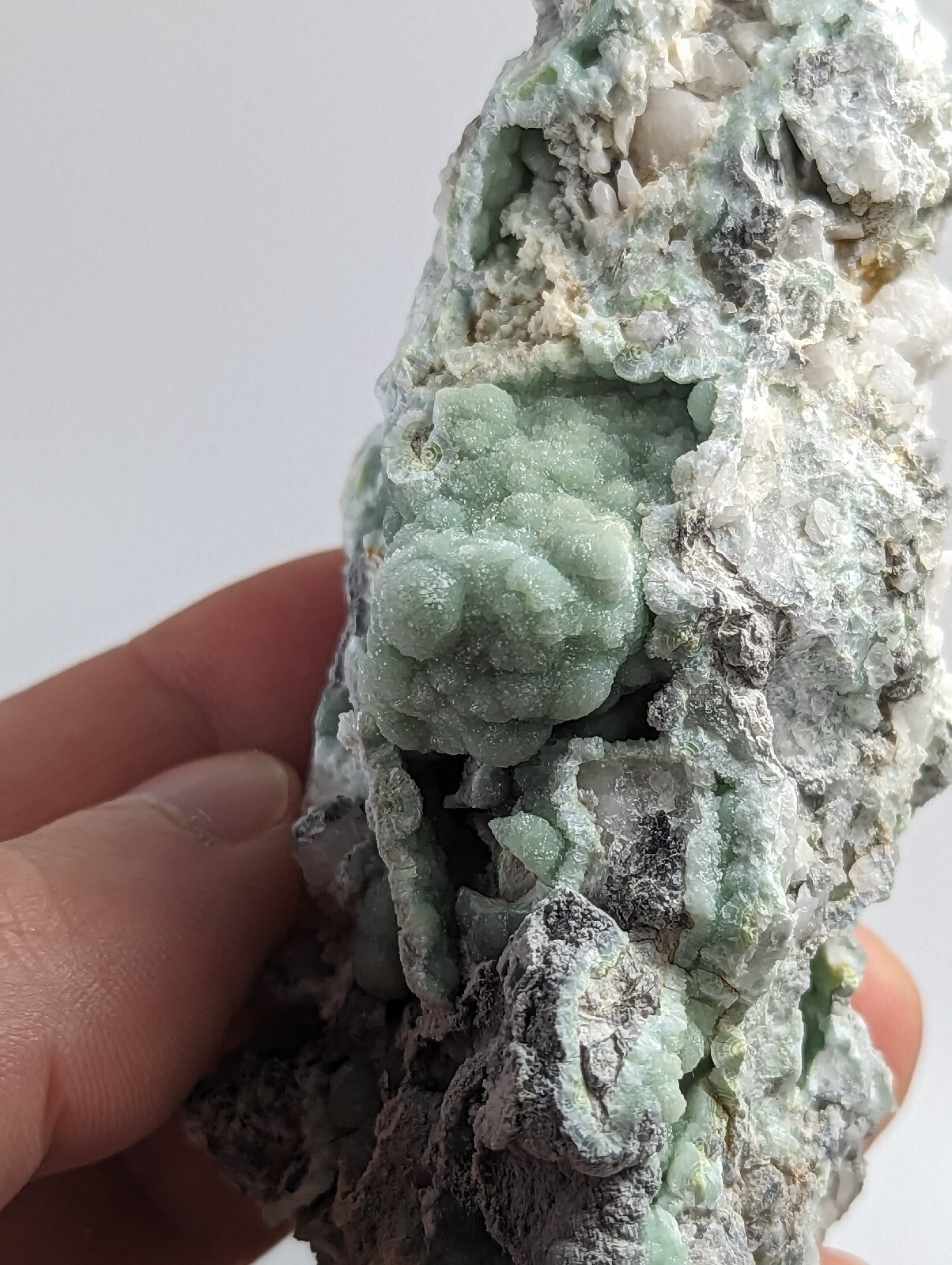 A textured, light green mineral specimen with a rough, crystalline surface and patches of white and gray matrix.