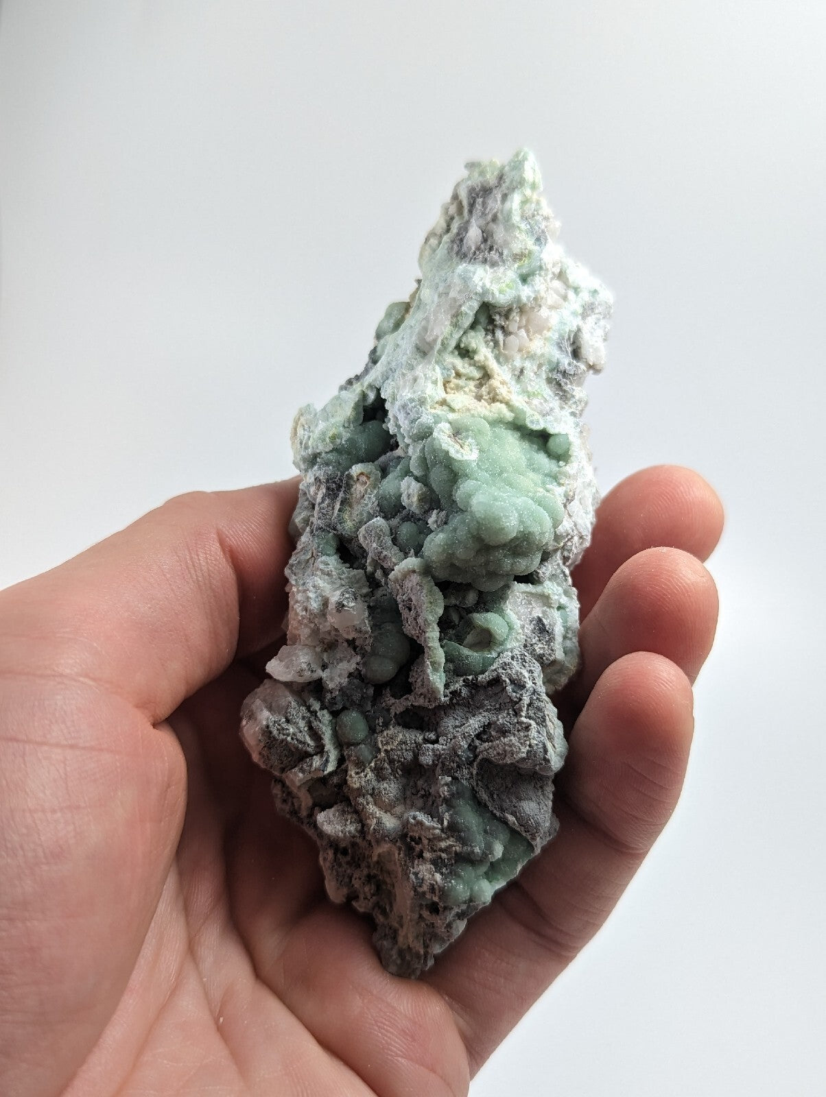 A hand holds a textured, light green and gray mineral specimen with rounded nodules.