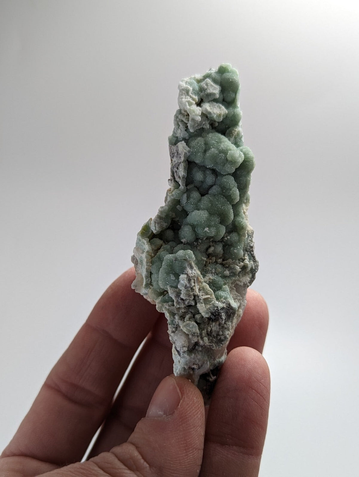A hand holds a striking green mineral specimen with a textured, bumpy surface and white crystalline patches.