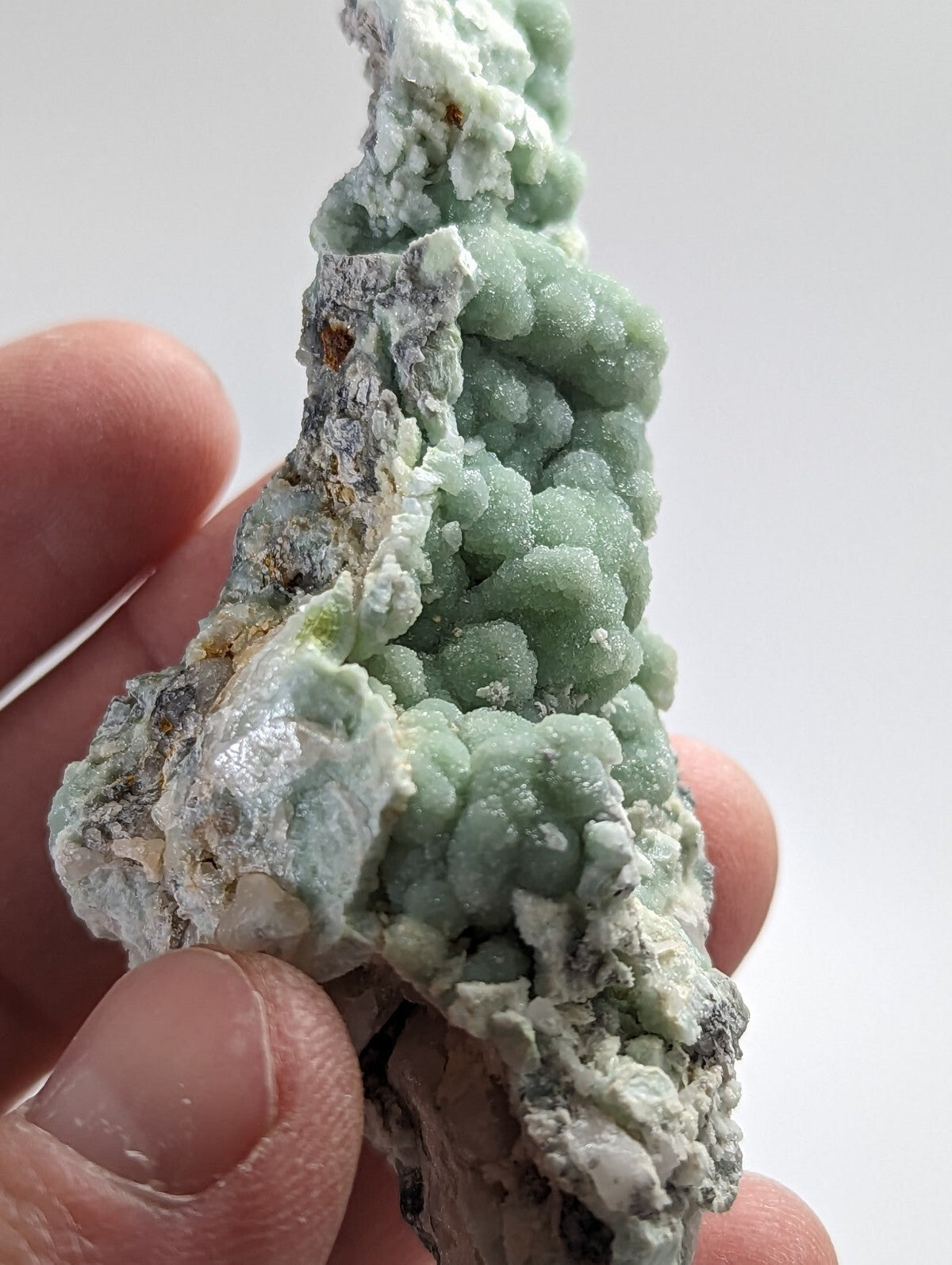A hand holds a striking light green, bumpy mineral specimen with white and gray matrix.