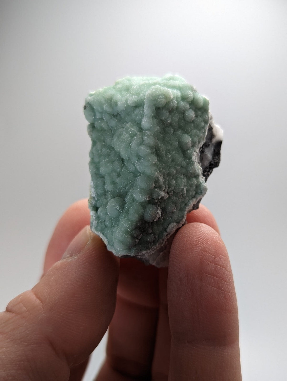 A light green, textured mineral specimen with a bumpy surface and some dark patches.