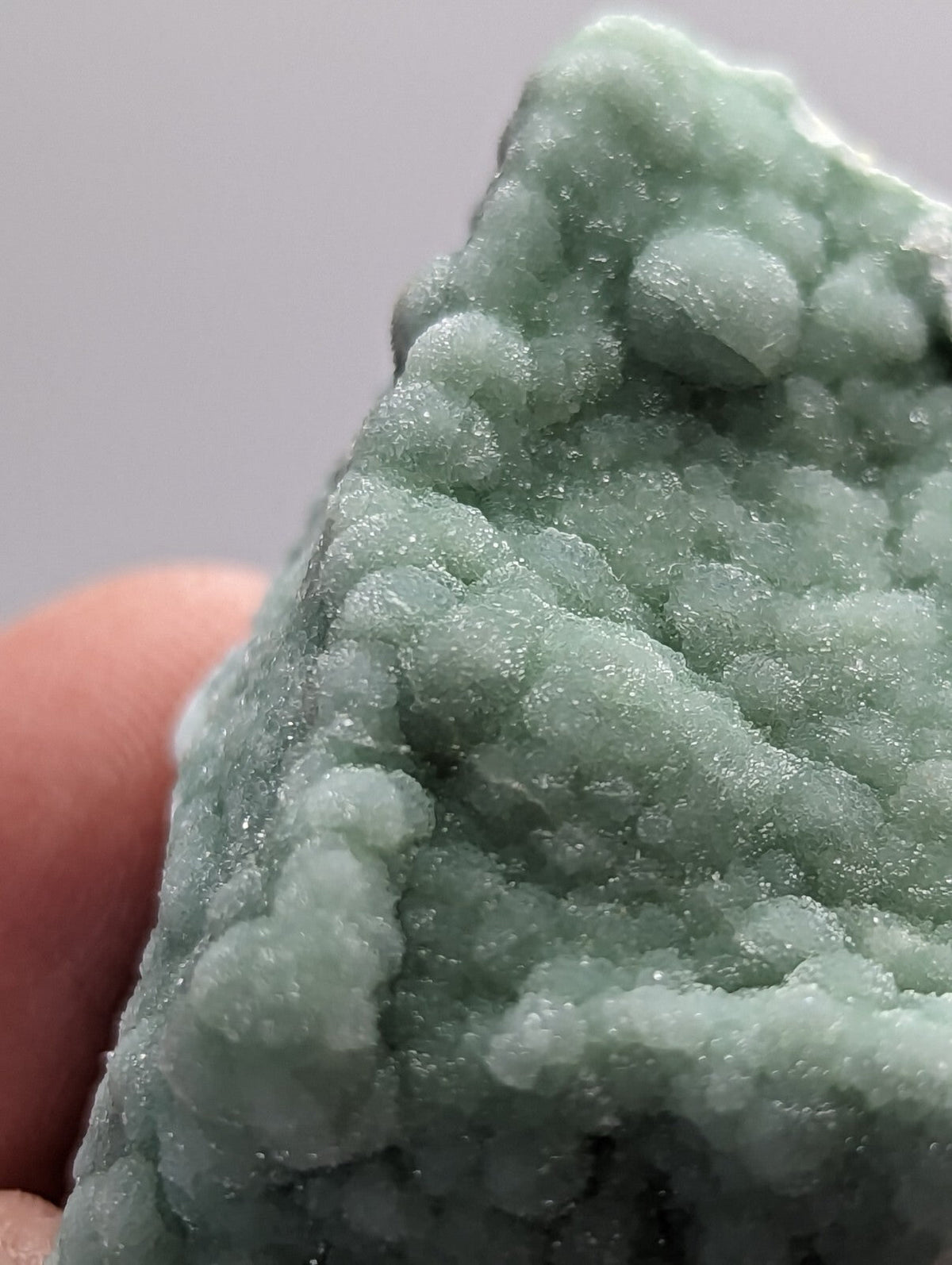 A textured, pale green mineral specimen with a crystalline, bubbly surface.