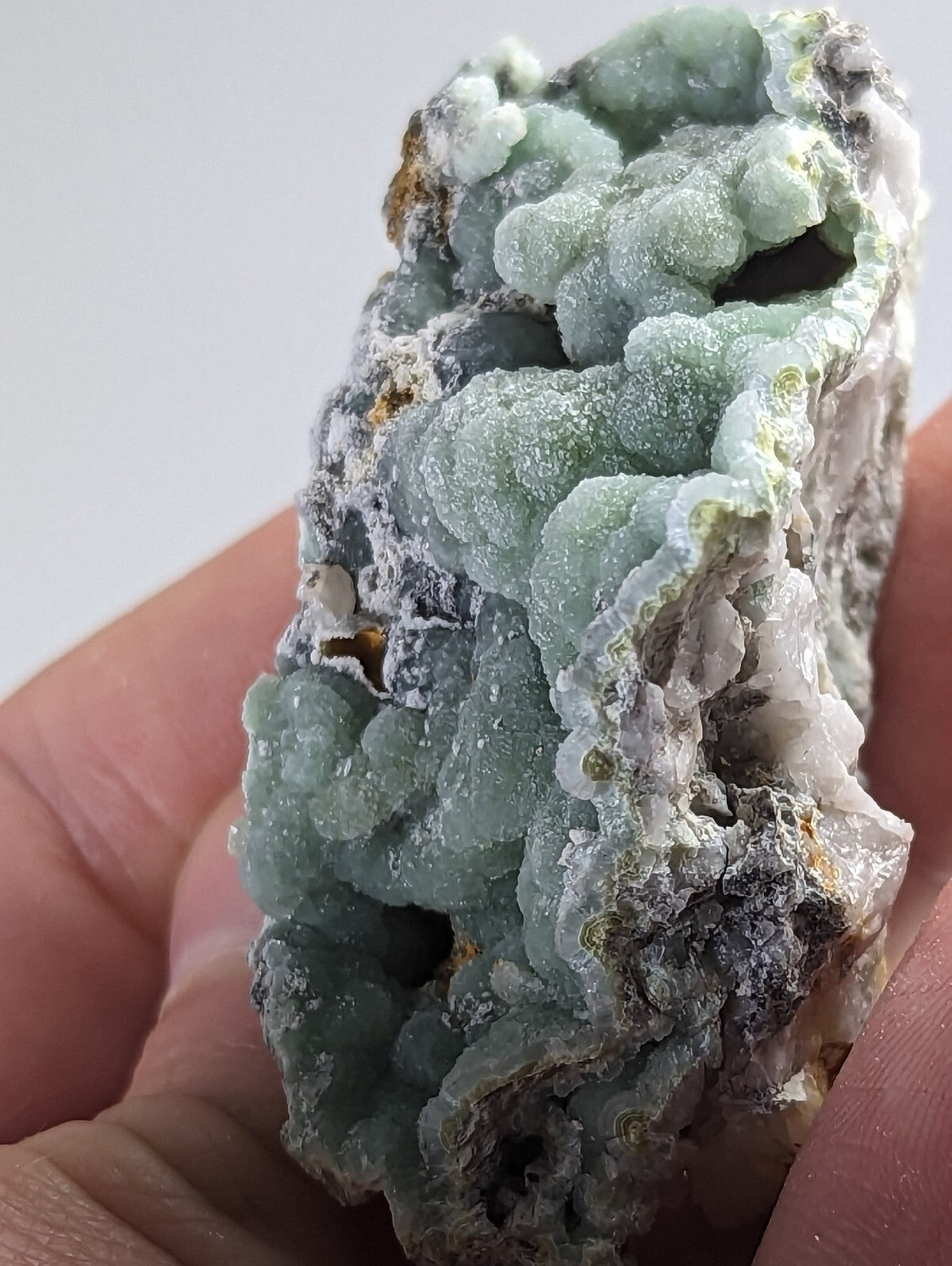 A hand holds a rough, irregularly shaped mineral specimen featuring translucent light green crystals with white and gray matrix material.