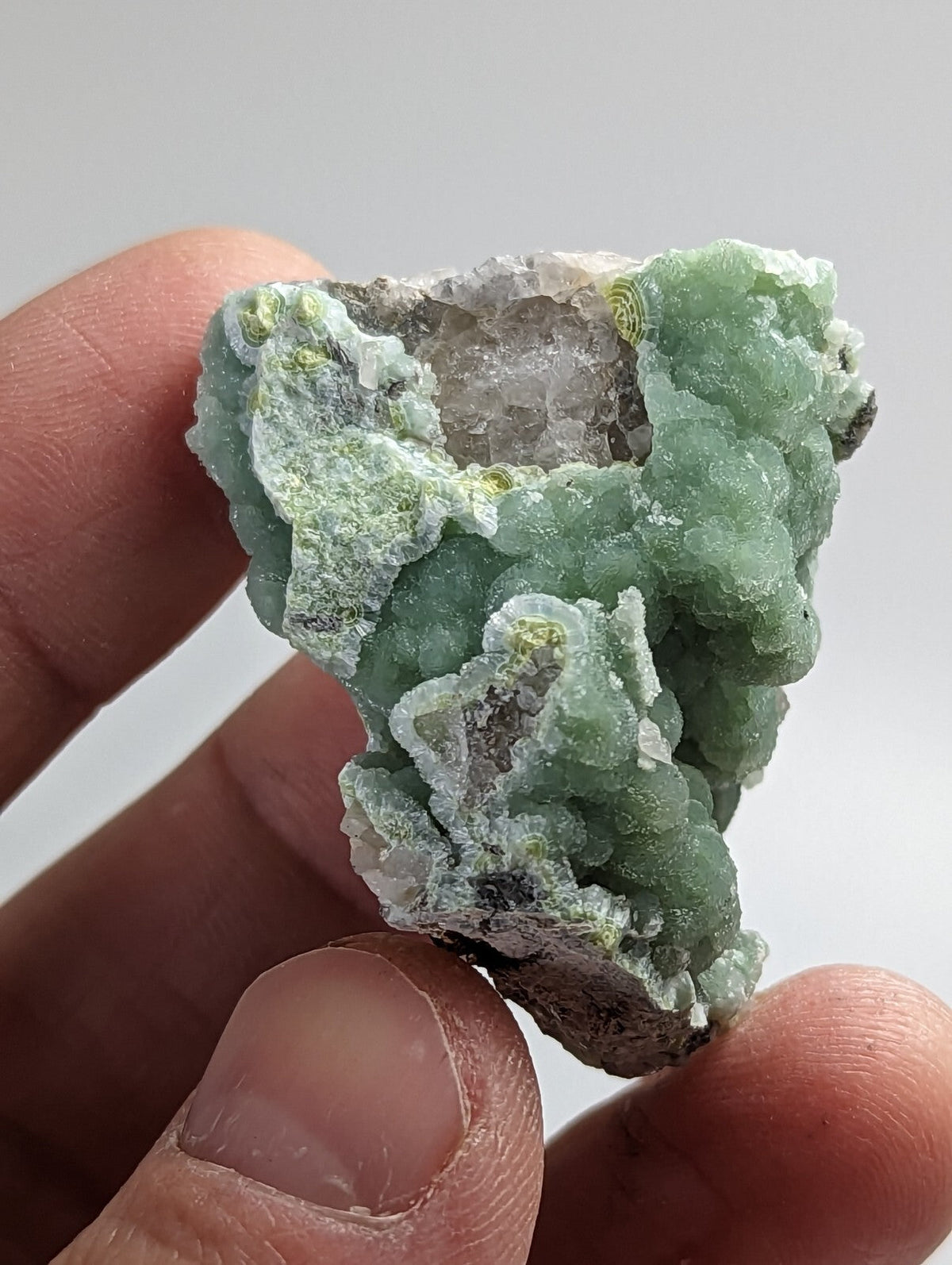 A hand holds a green, crystalline mineral specimen with a rough, textured surface and translucent patches.