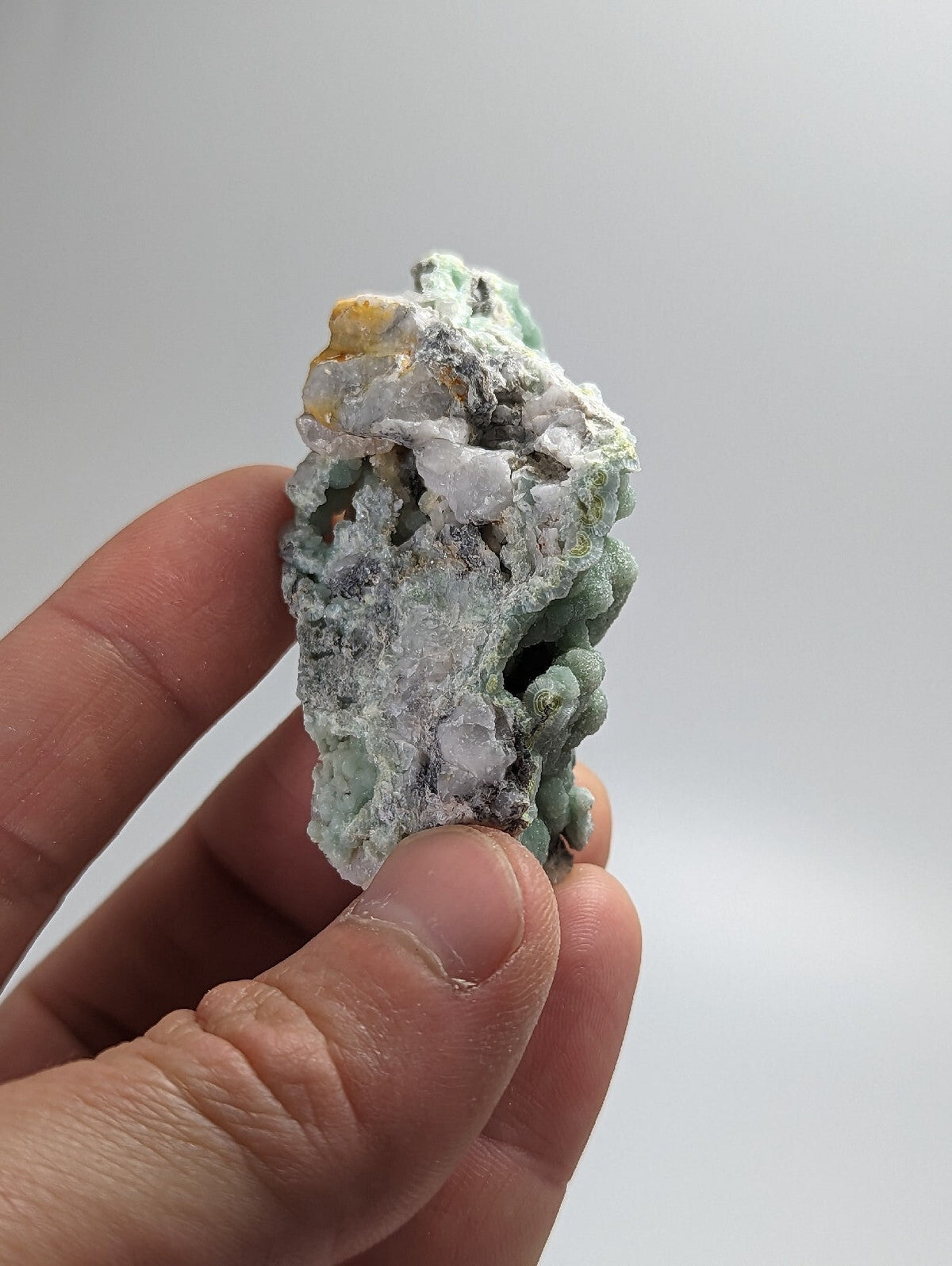 A textured, light green and white mineral specimen with patches of yellowish crystals.