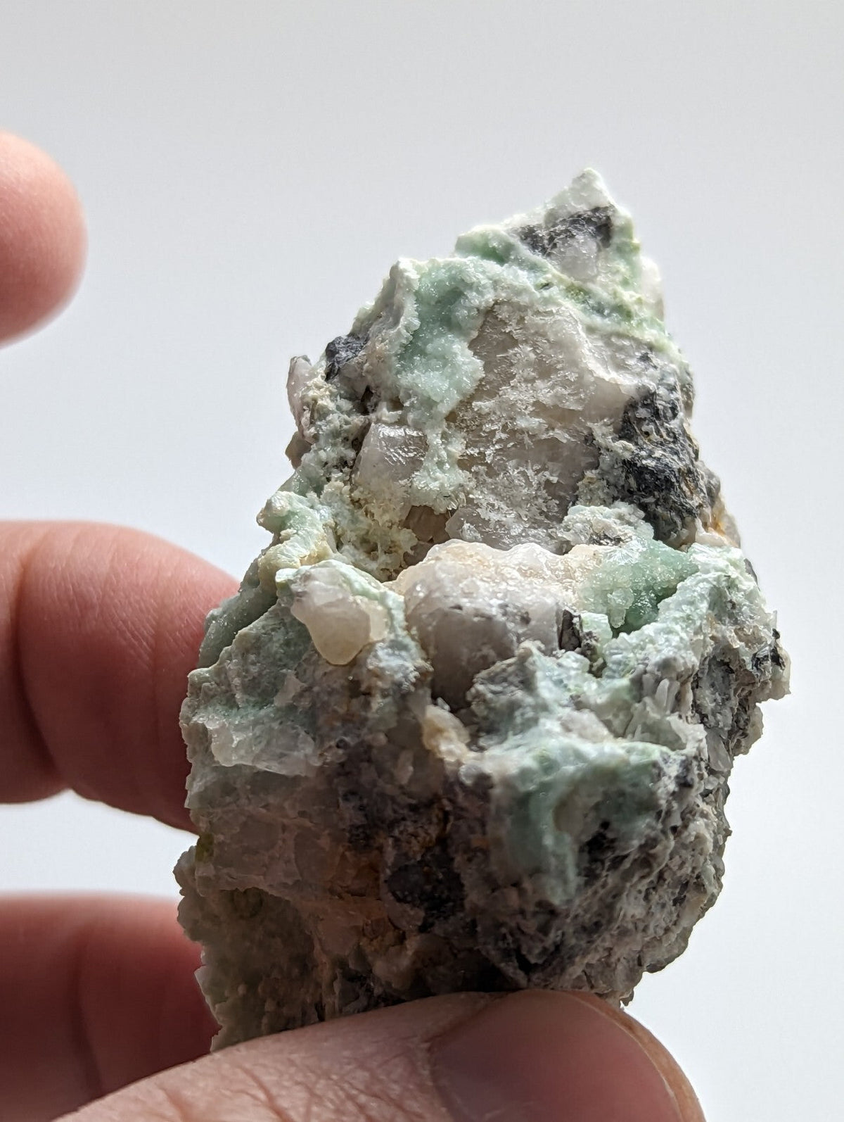 A rough, irregularly shaped mineral specimen with a mix of pale green and white crystalline formations set against darker gray matrix.