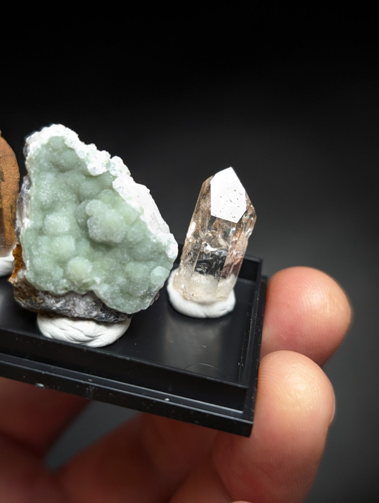 A translucent, faceted quartz crystal with a pointed tip and subtle internal inclusions sits on a white base within a black display tray.