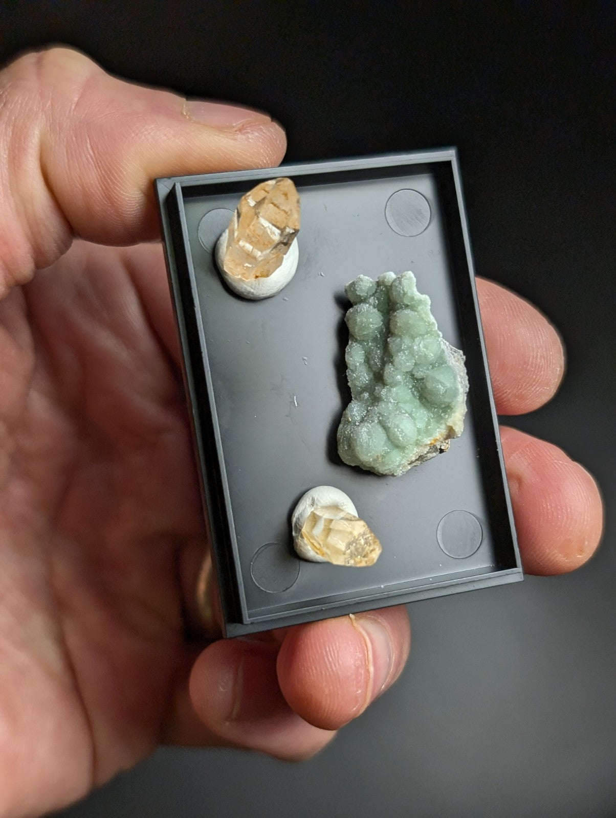 Black rectangular display tray holding three mineral specimens.