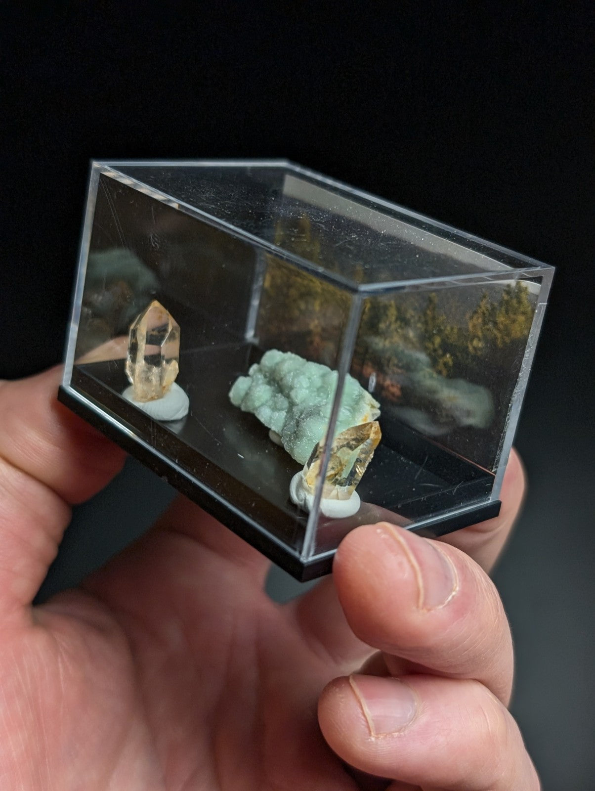 Clear acrylic display case holding two mineral specimens on white circular bases.