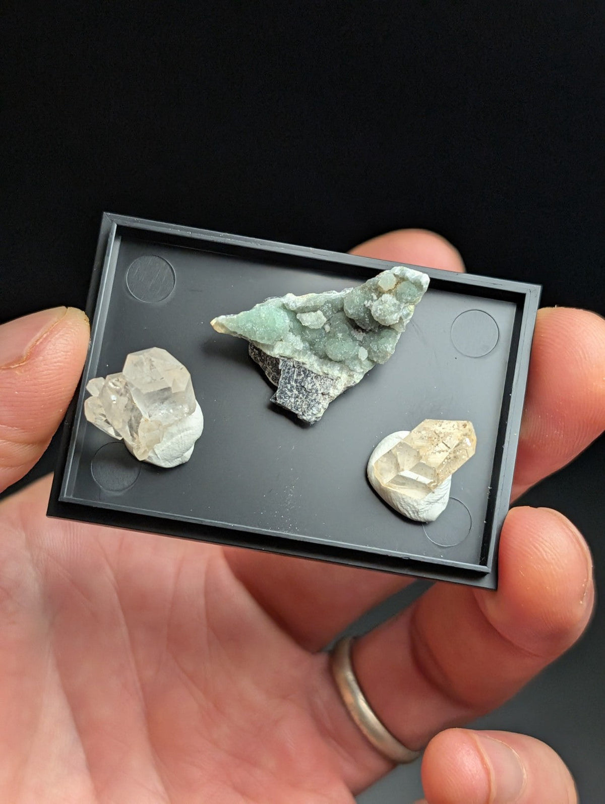 Black rectangular display tray holding three distinct mineral specimens.