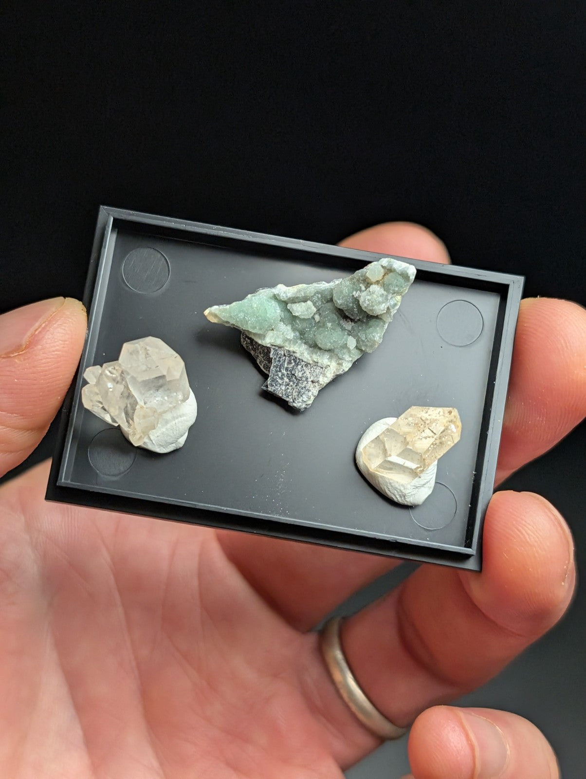 Black rectangular display tray holding three distinct mineral specimens.