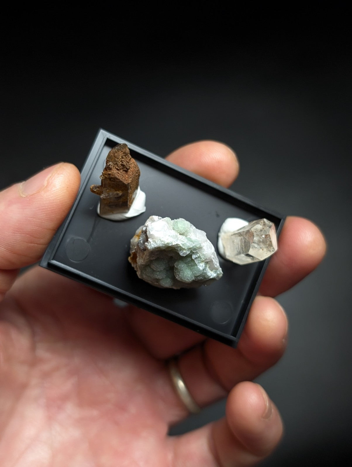 Black rectangular display tray holding three distinct mineral specimens.