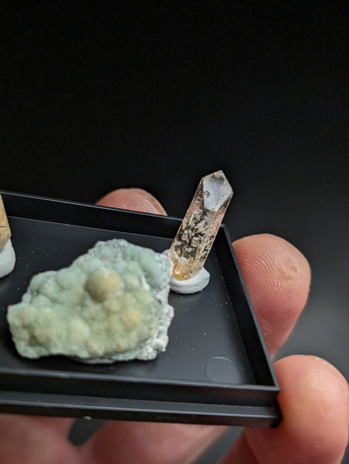 A translucent amber-colored crystal with a pointed tip, mounted on a small white base.