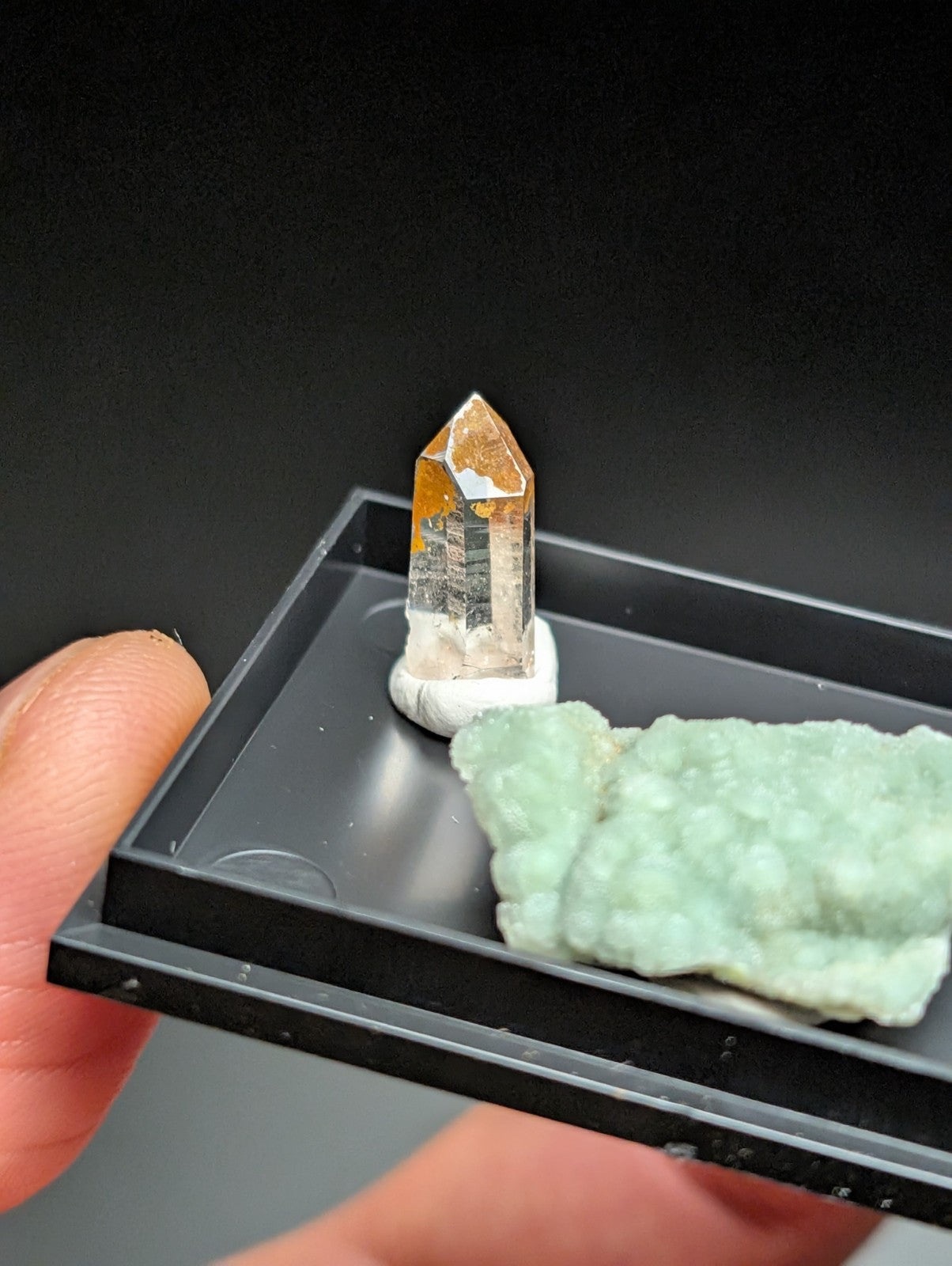 A translucent orange and clear quartz crystal with a pointed tip, mounted on a white base.