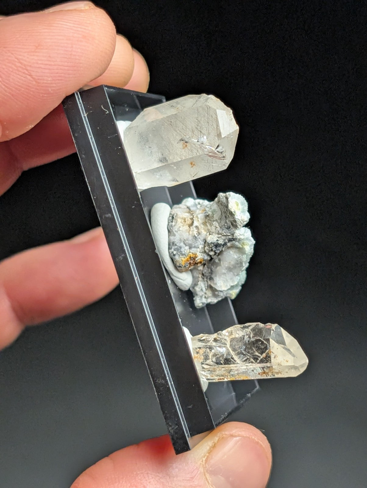 A clear, faceted quartz crystal mounted in a black display case alongside other mineral specimens.