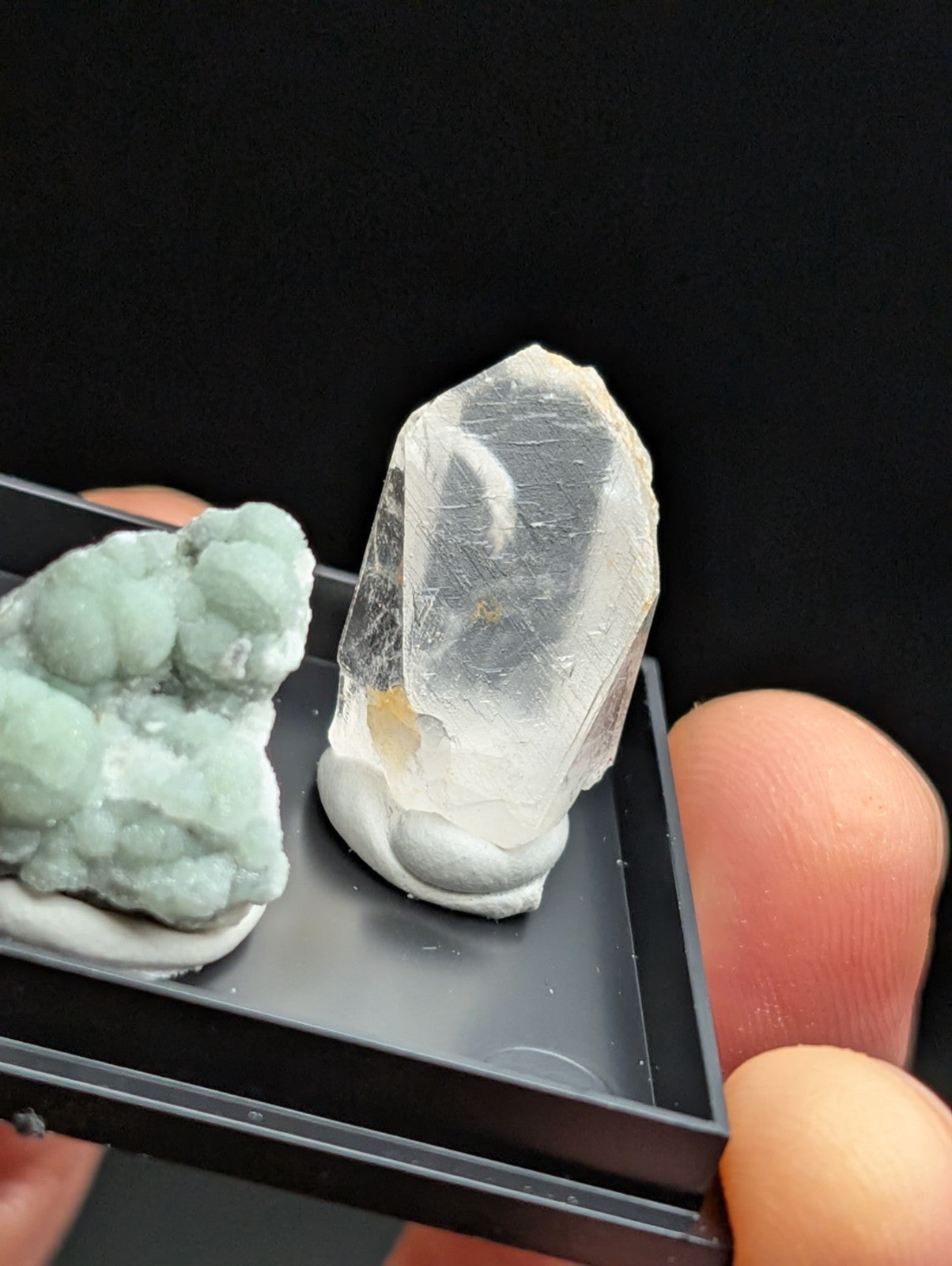 A translucent, clear quartz crystal with a pointed tip and visible internal inclusions rests on a white base within a black display tray.