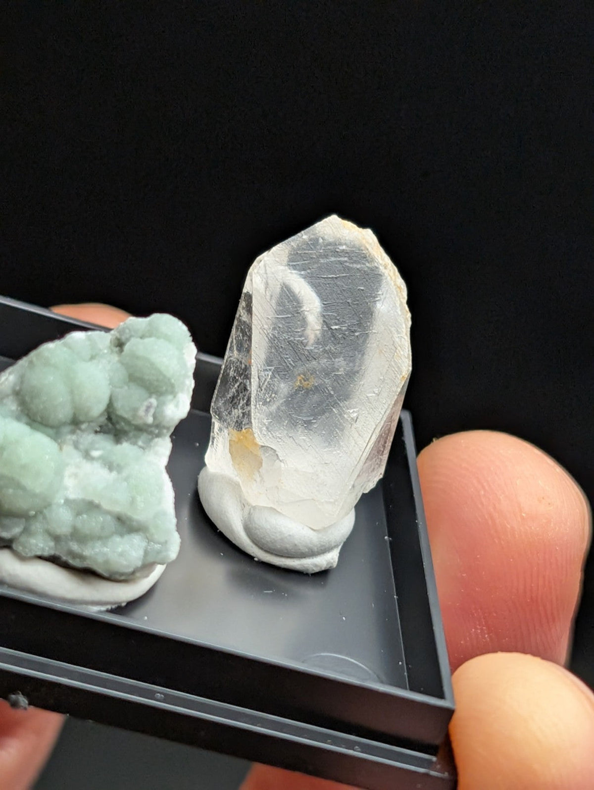 A translucent, clear quartz crystal with a pointed tip and visible internal inclusions rests on a white base within a black display tray.