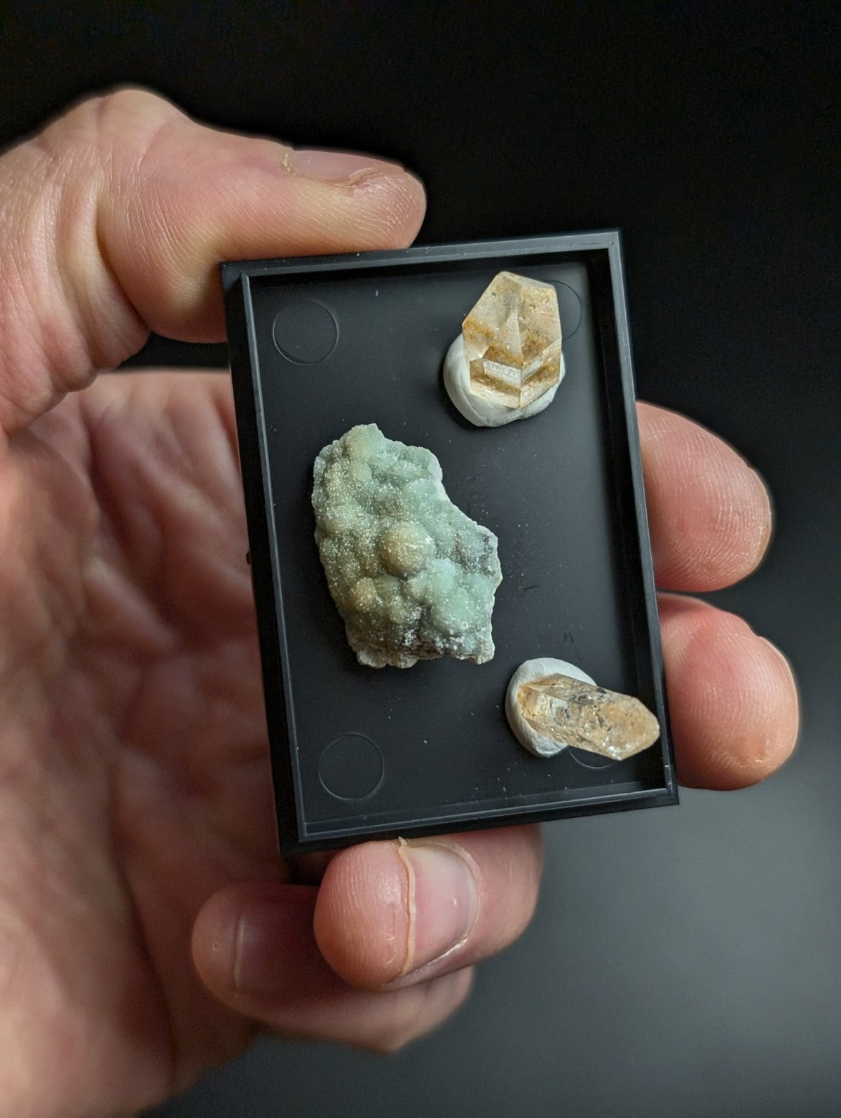 Black rectangular display case holding three mineral specimens.
