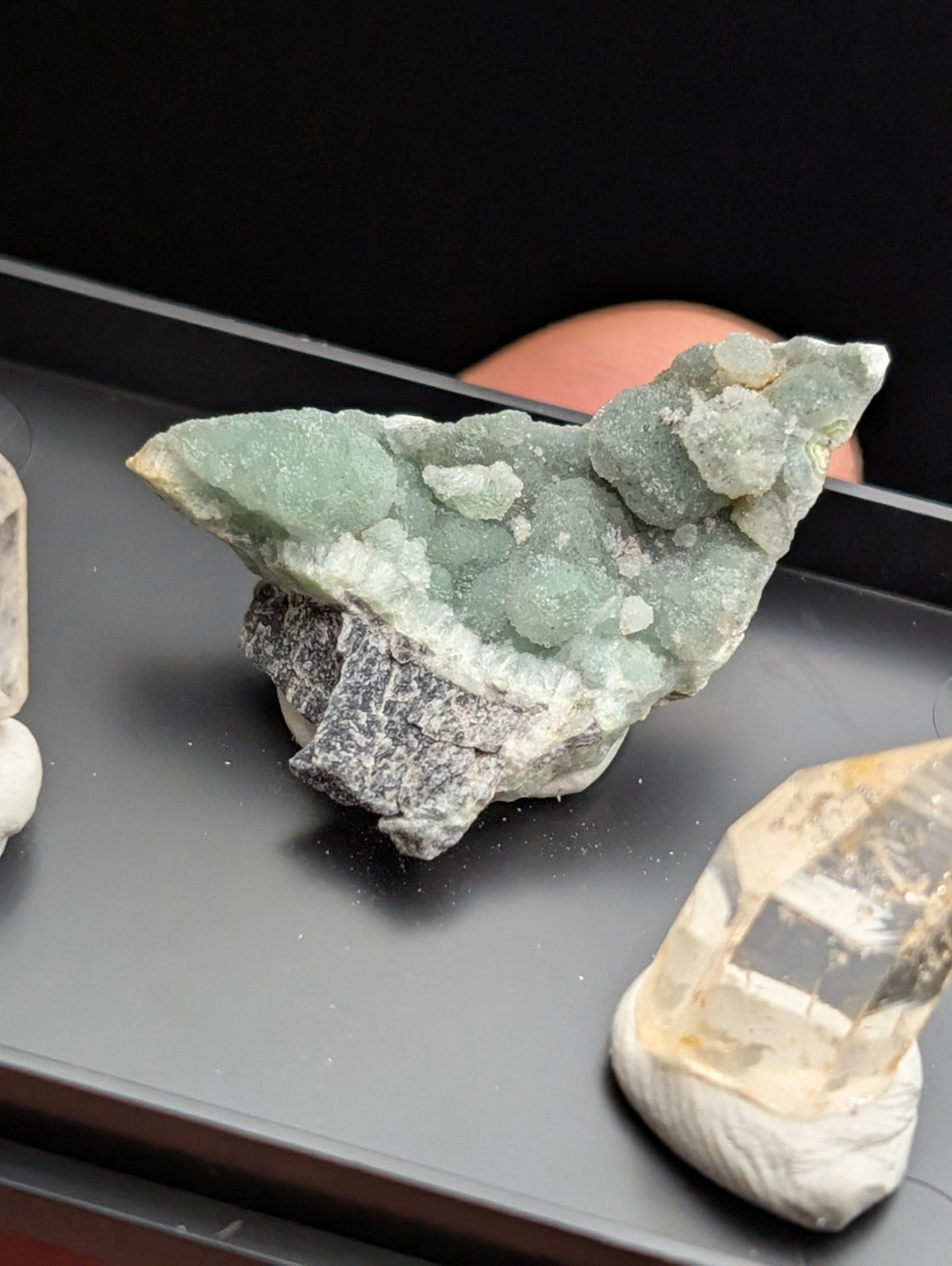 A greenish-blue mineral specimen with a crystalline, textured surface and a rough, dark gray base.