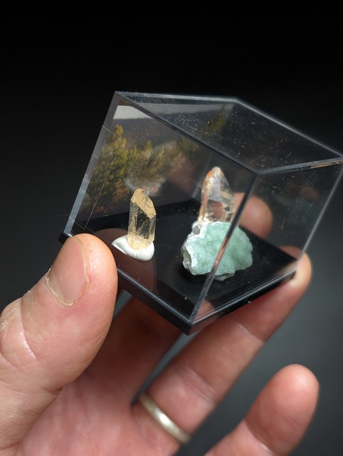 透明立方体展示盒内陈列着两件矿物标本，一件是黄褐色晶体立于白色底座上，另一件为青绿色岩石。