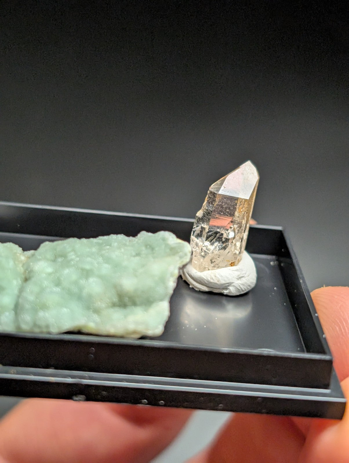 A translucent golden quartz crystal with a pointed tip, displayed on a white pedestal within a black tray.