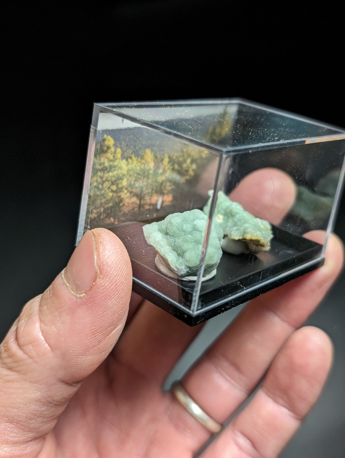 A translucent green mineral specimen displayed in a clear acrylic cube with a black base.