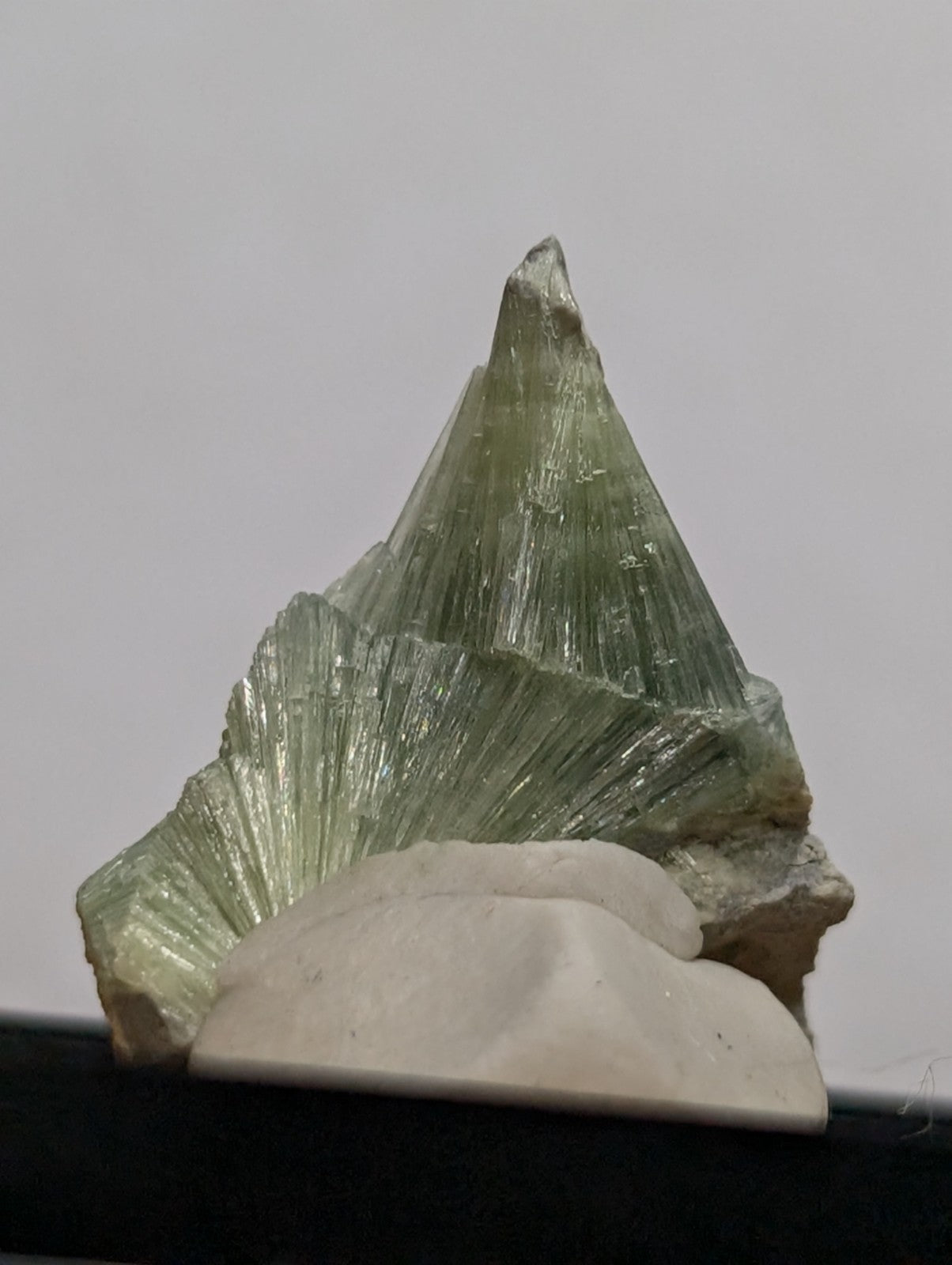 A translucent green mineral specimen with a pointed, fan-like crystalline structure.