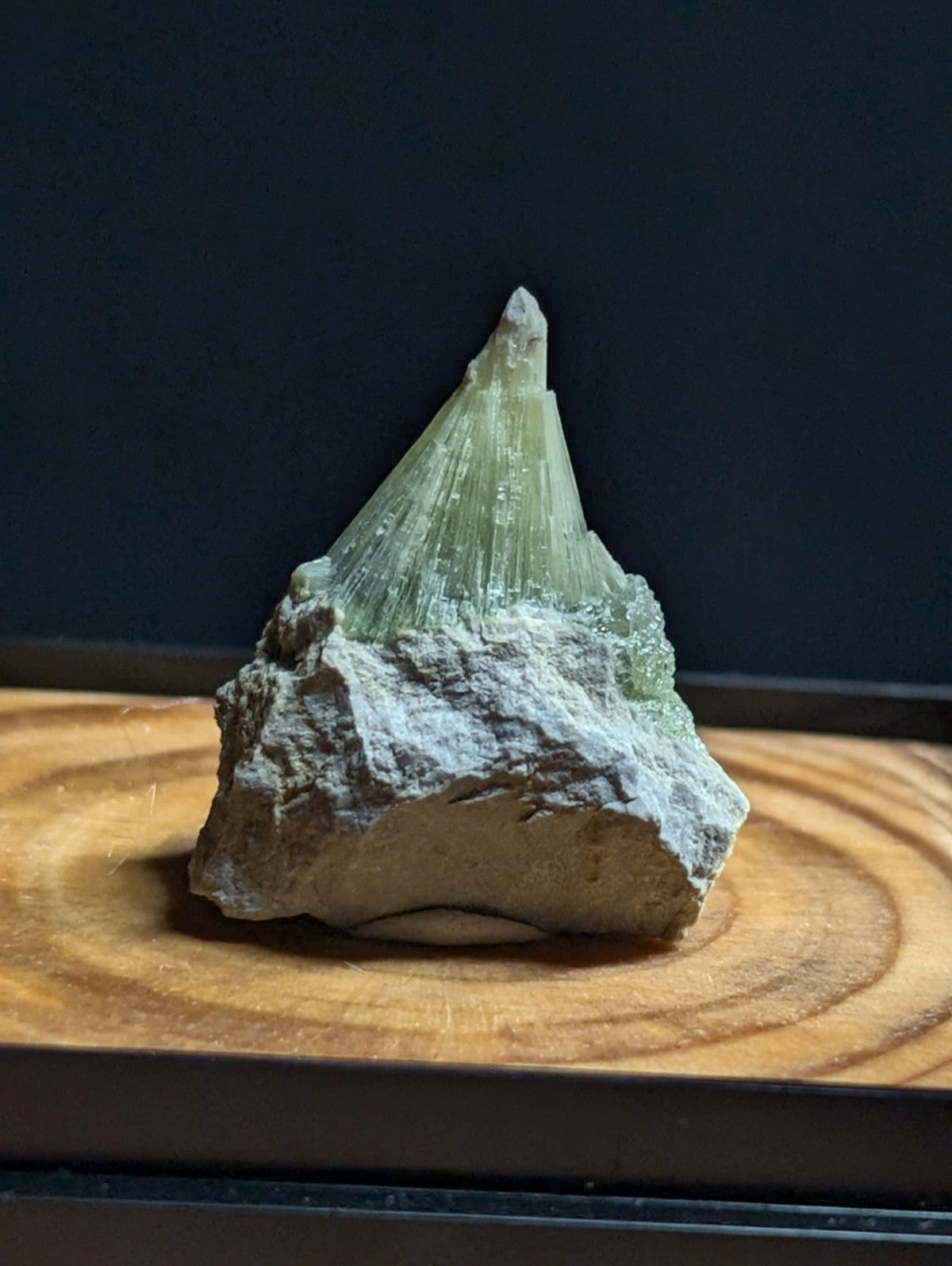 A translucent green mineral crystal with sharp, radiating facets emerges from a rough, grayish rock base.