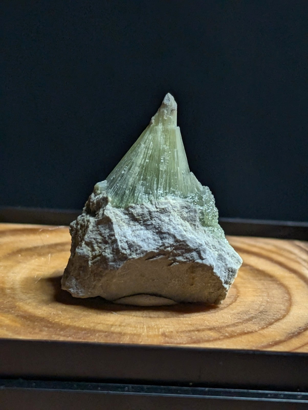 A translucent green mineral crystal with sharp, radiating facets emerges from a rough, grayish rock base.
