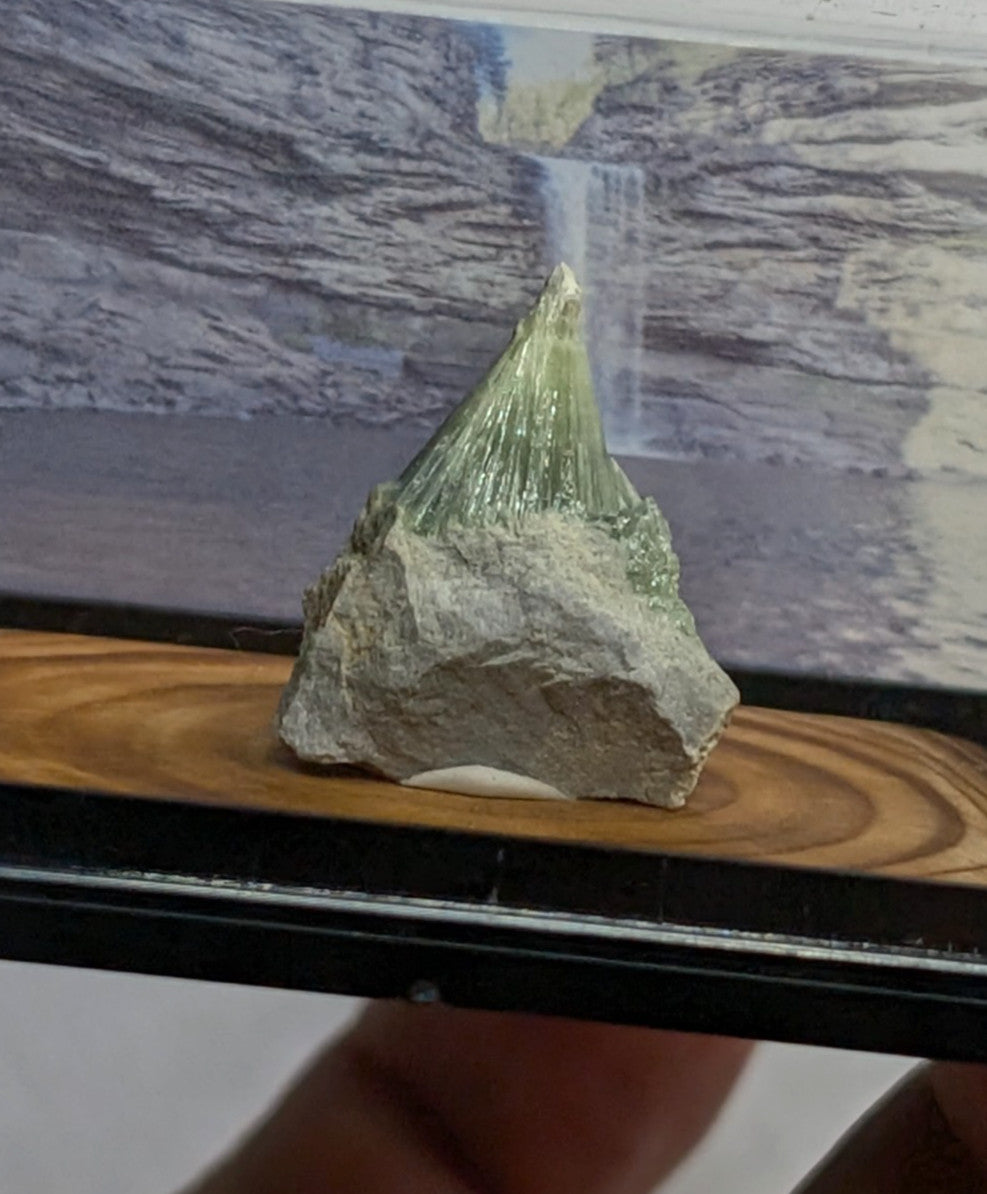 A translucent green mineral specimen with a crystalline, pointed top and rougher grayish base.