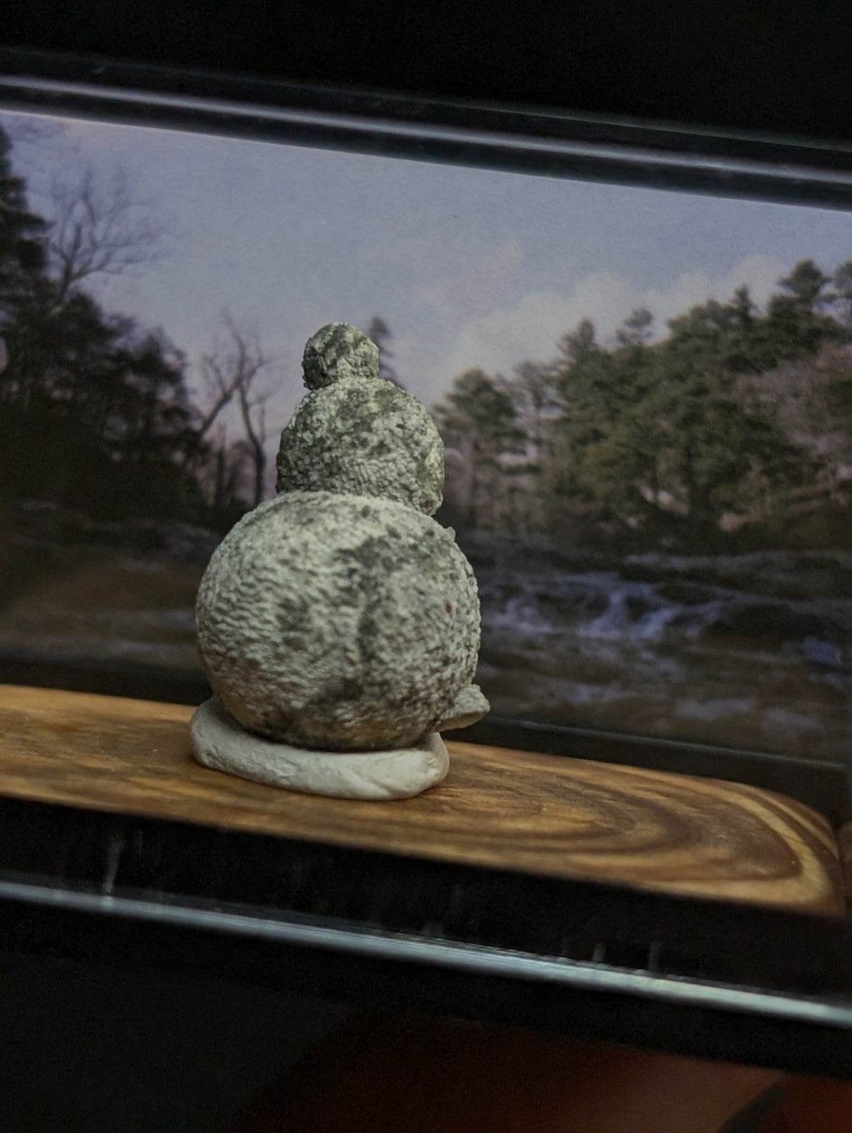 Gray, textured stone figurine of a seated figure with rounded form and small head.