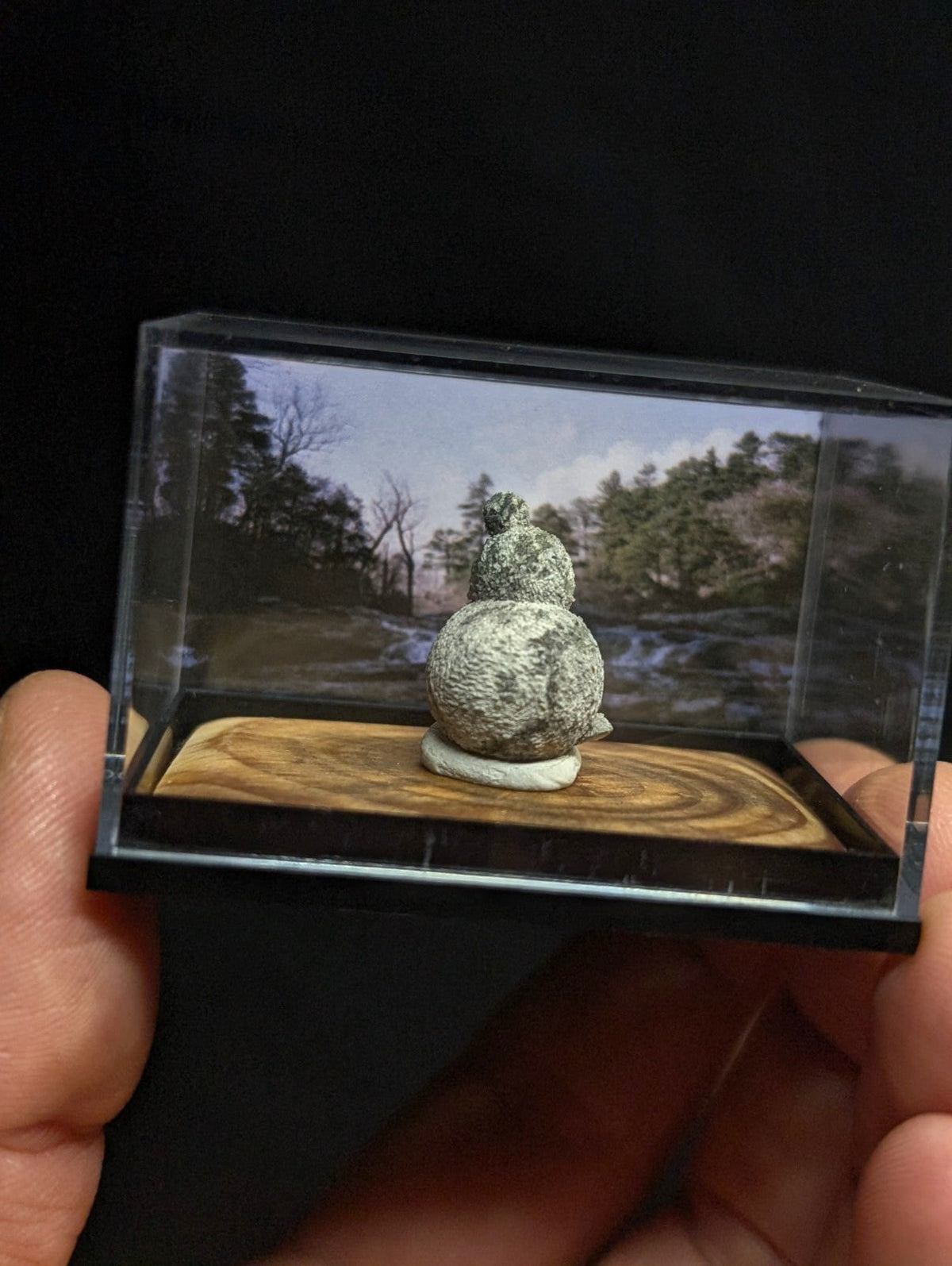 A miniature, textured green and white stone gourd sculpture displayed in a clear acrylic display case.
