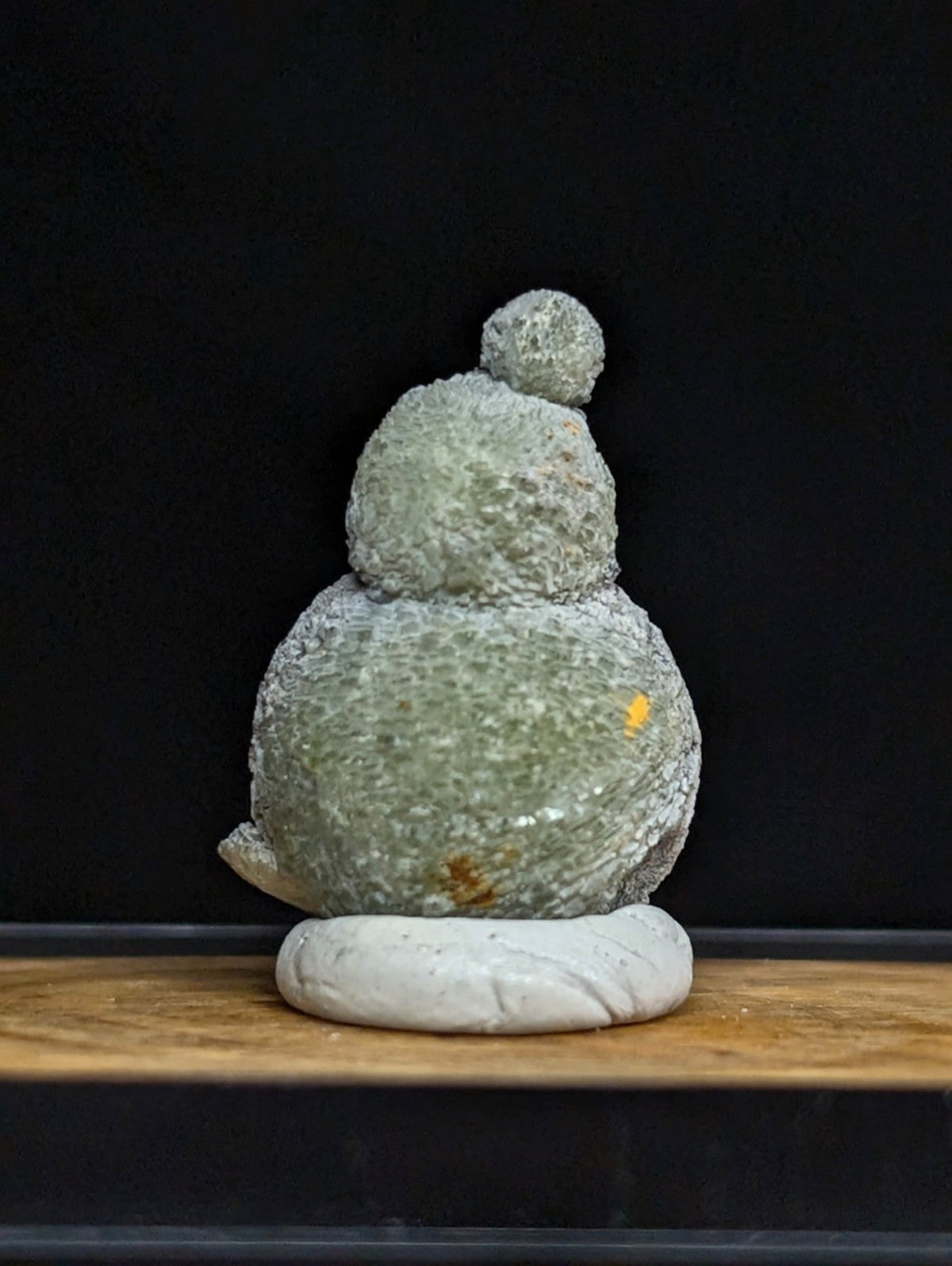 A textured, light green stone sculpture shaped like a stacked snowman with a small rounded top and standing on a white marble base.