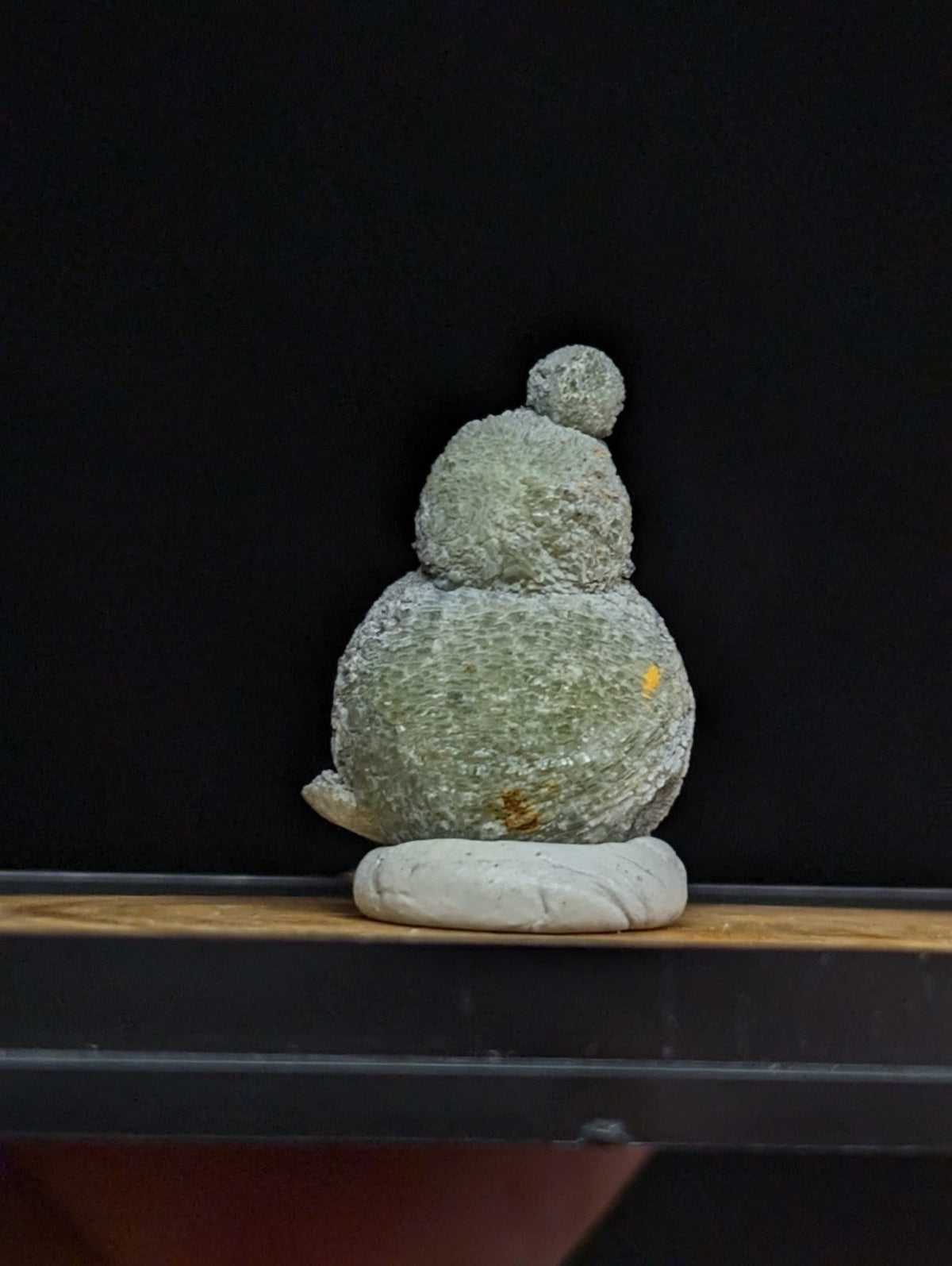 A textured, moss-green stone figurine with a rounded body and small spherical top.