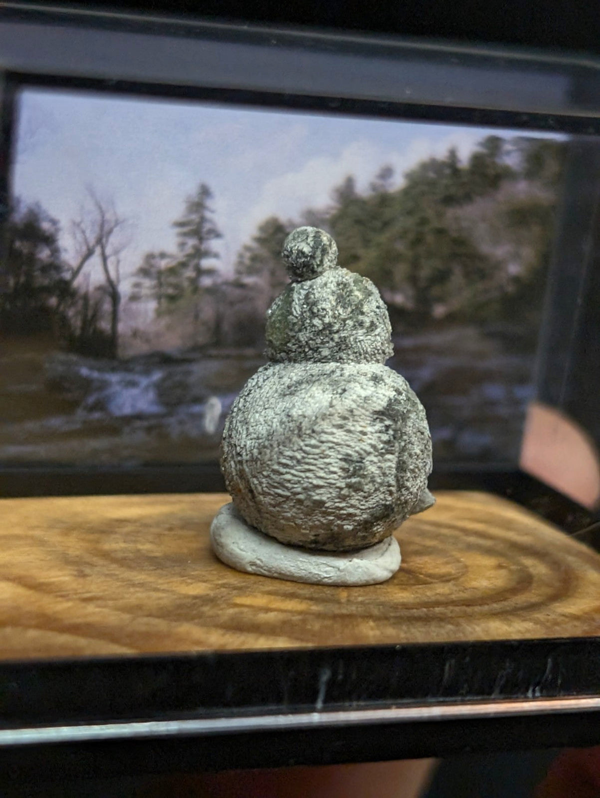 A textured, gray stone figurine shaped like a snowman with a rounded body and top hat.