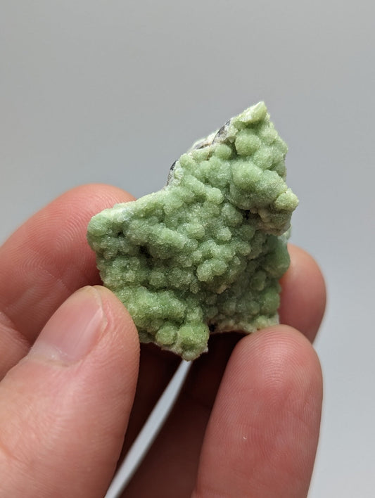 A light green, textured mineral specimen with a rough, crystalline surface held between fingers.