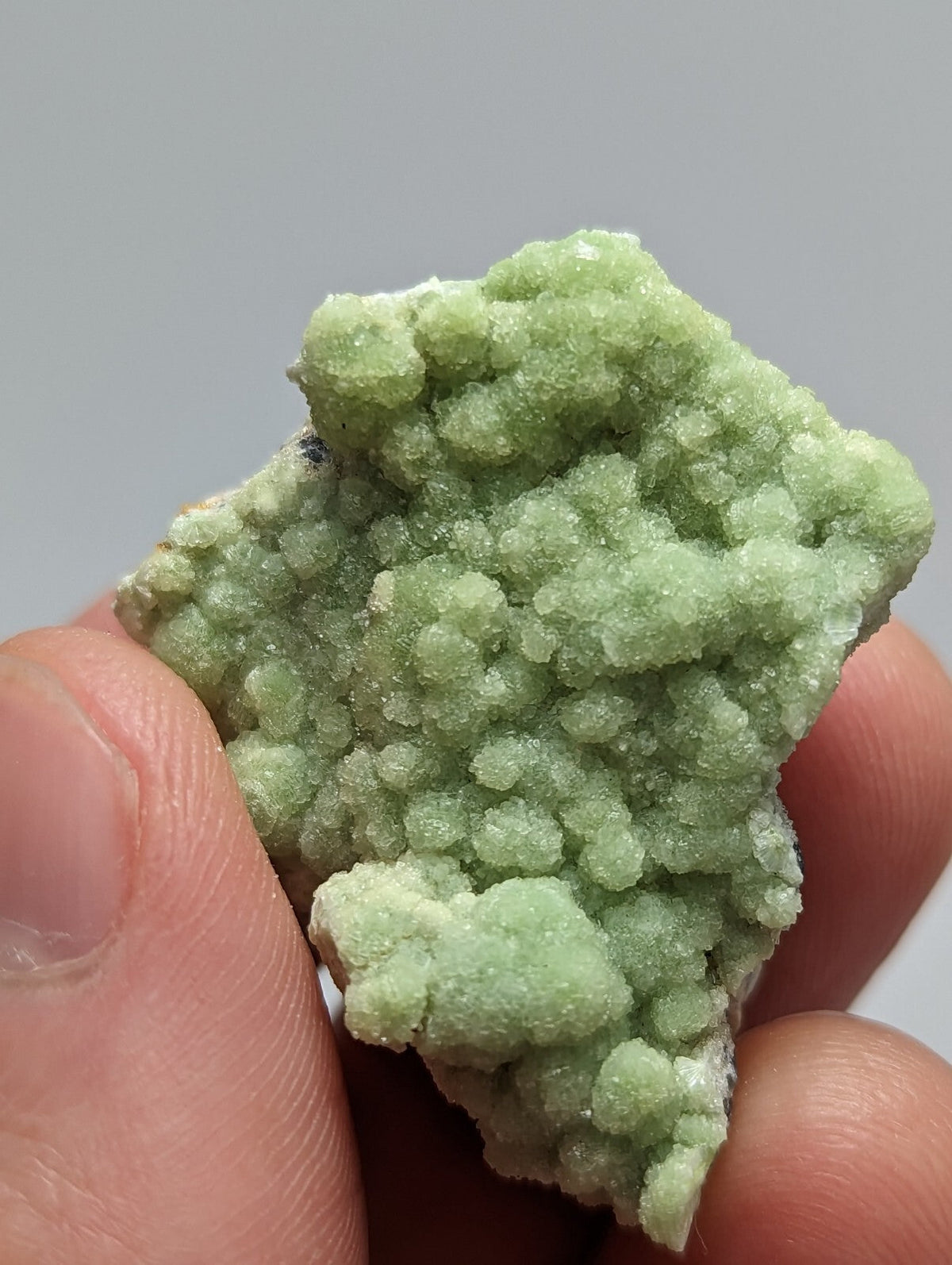 A pale green, crystalline mineral specimen with a rough, textured surface held in someone’s hand.