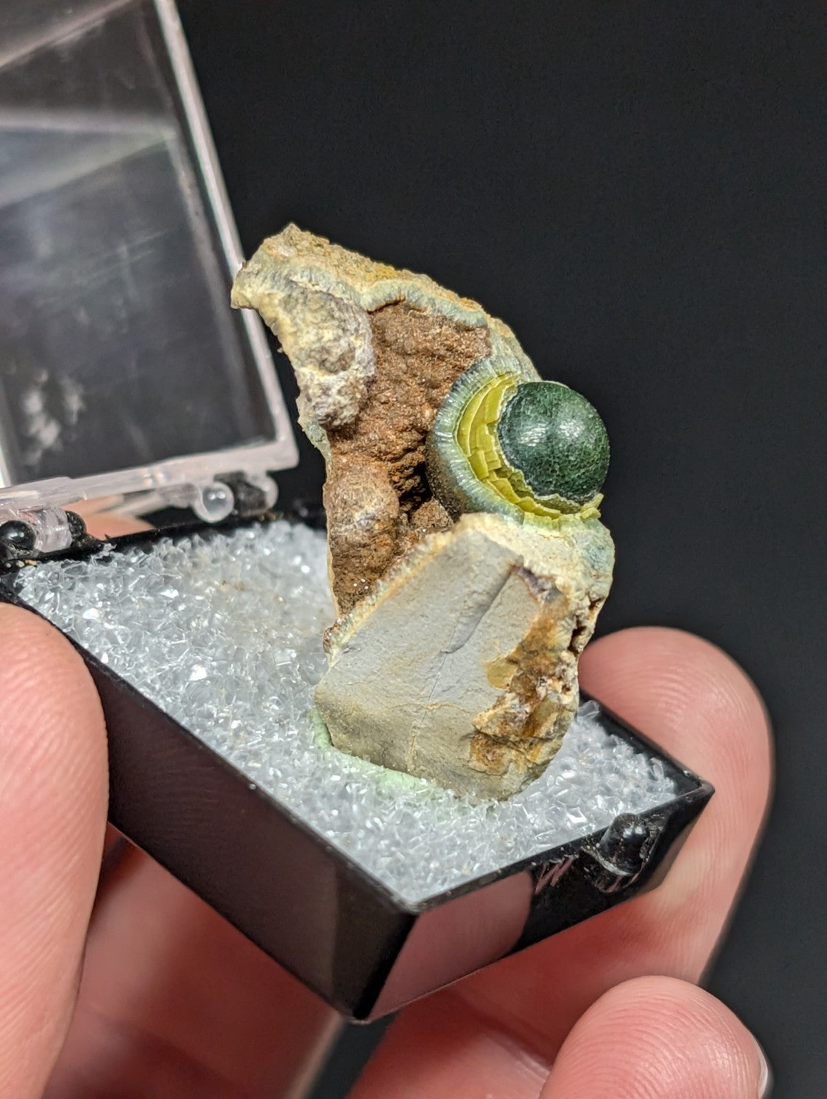 A polished green spherical mineral nestled within a rugged, earth-toned rock matrix.