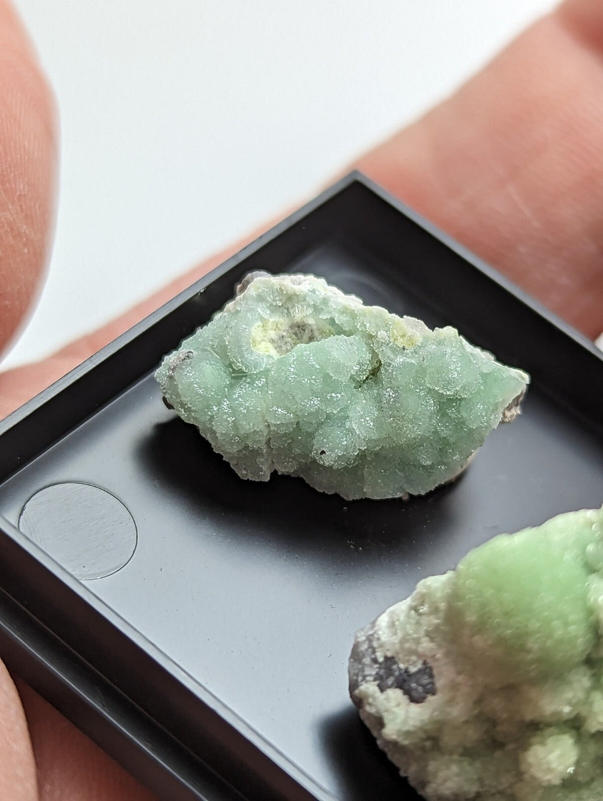 A pale green, crystalline mineral specimen with a rough, textured surface and subtle yellowish patches.