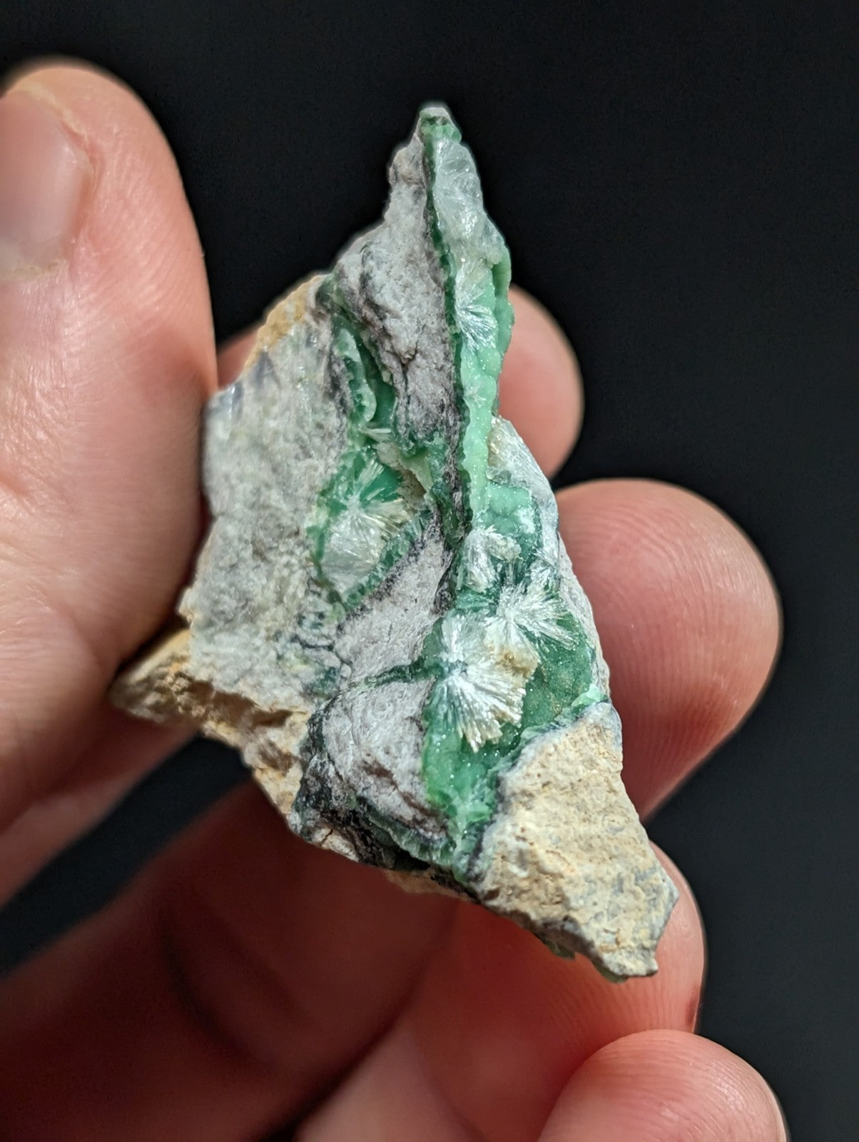 A hand holds a rough, irregularly shaped piece of green and white mineral with visible crystalline formations.
